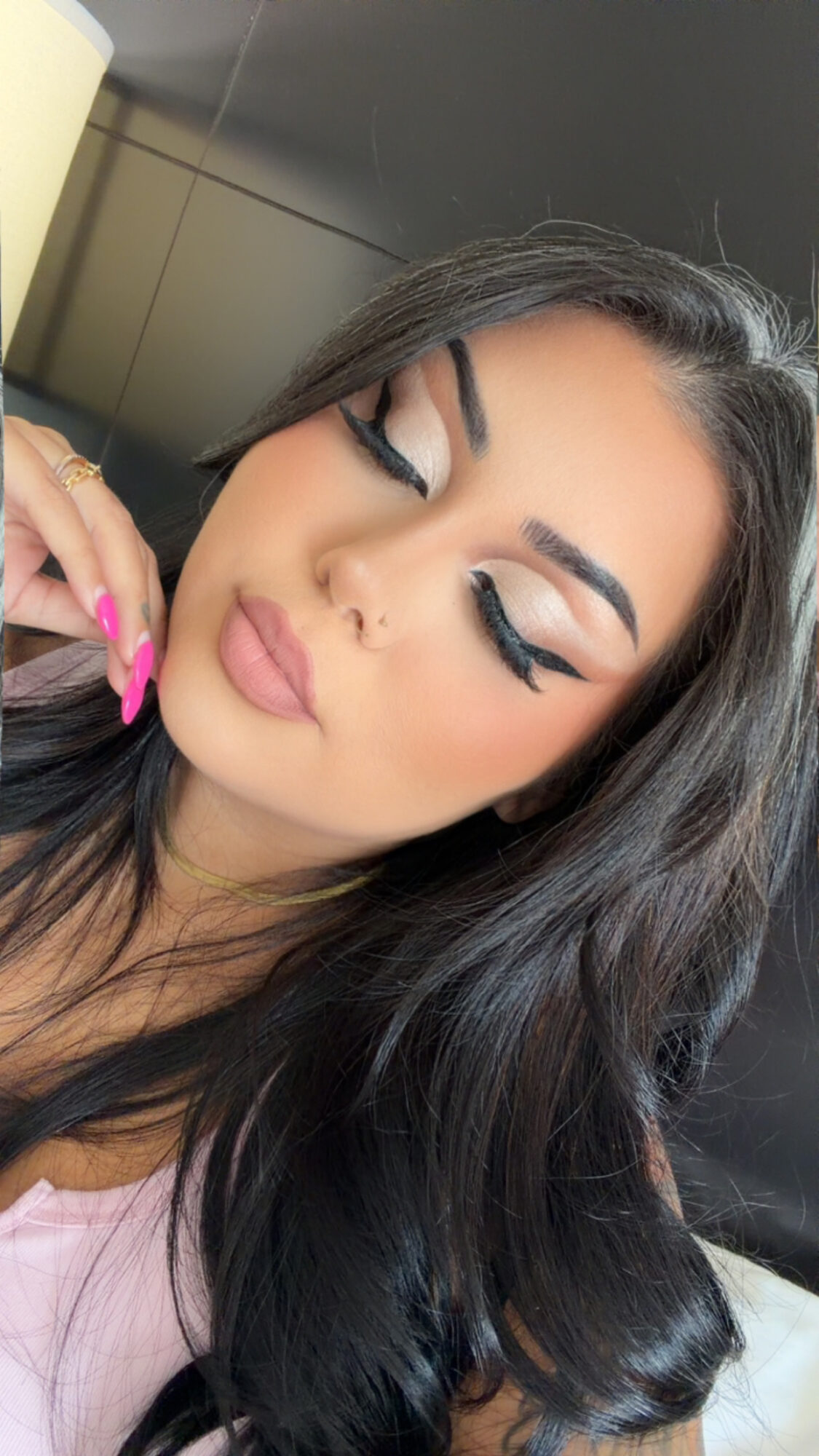 Close-up of a woman with makeup, long dark hair, and closed eyes, resting her face on her hand.