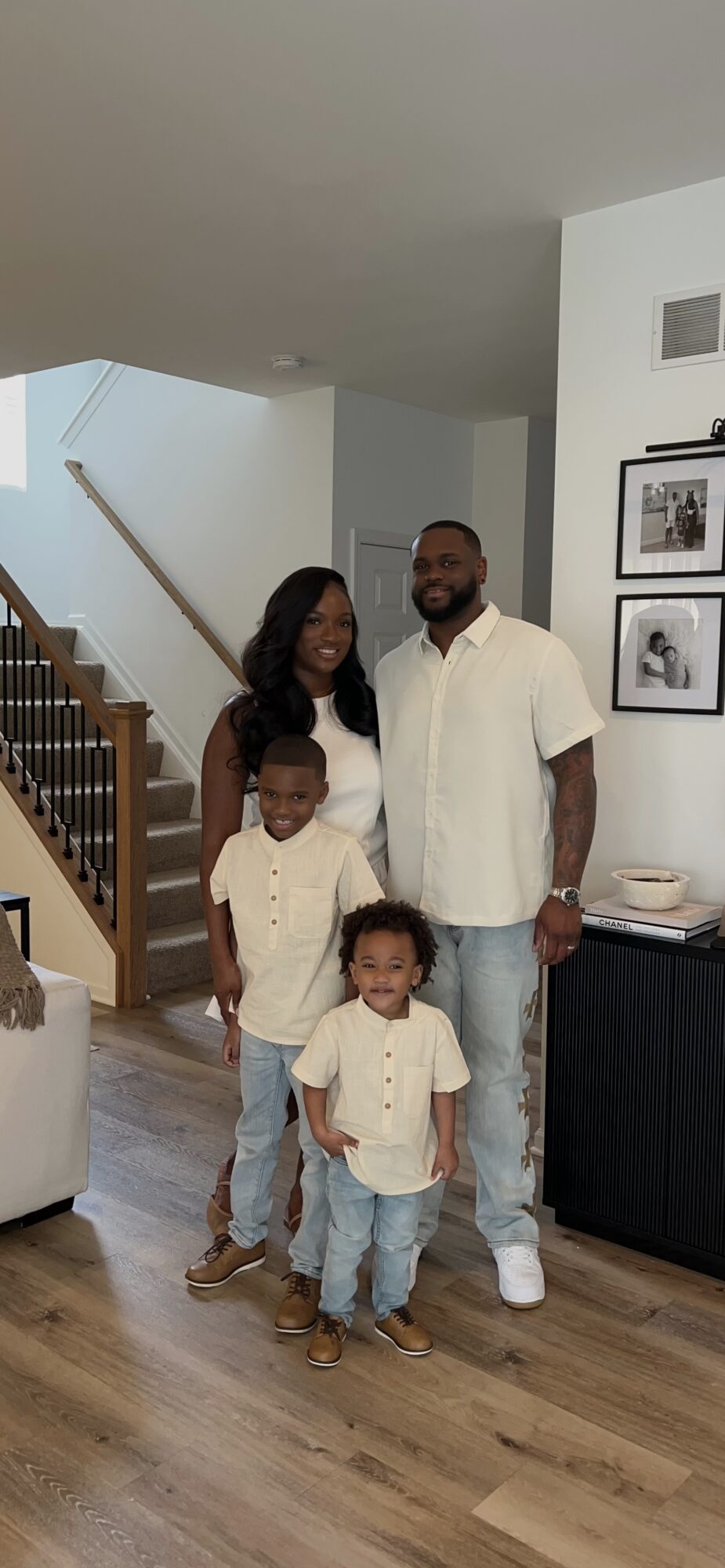 Family of four standing in a living room, smiling, with a staircase in the background.