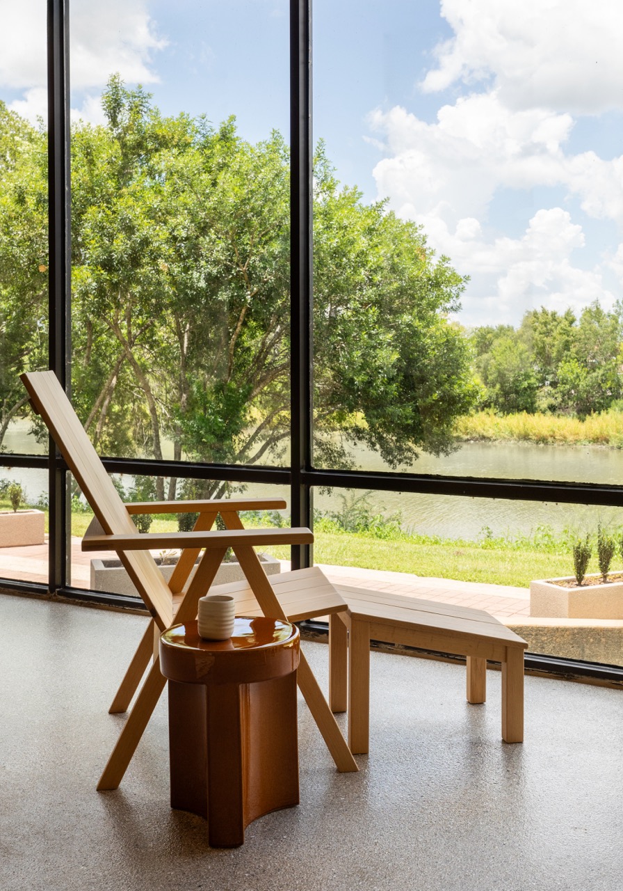 Indoor scene with wooden chair, small table, and a view of trees and sky through large glass windows.