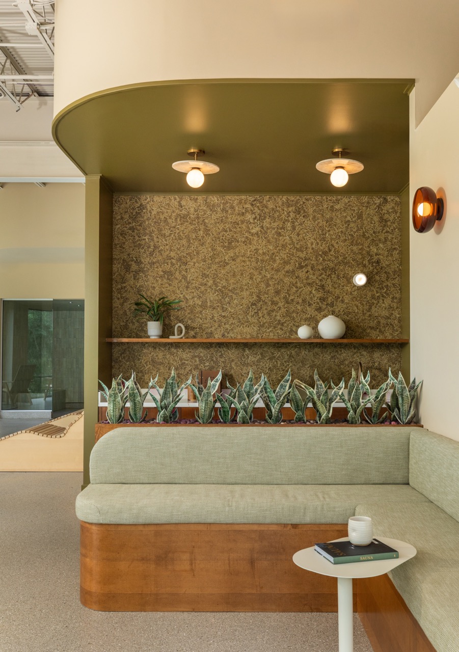 Corner seating area with a light green cushioned bench, wooden base, and a small white table with a cup and book, decorative shelf above.