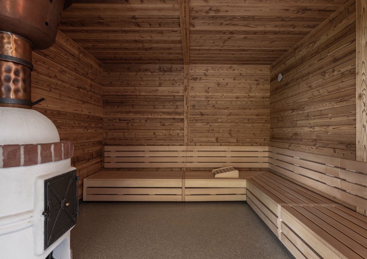Wood-paneled sauna with benches along two walls, corner seating, and a wood stove in the corner, carpeted floor.