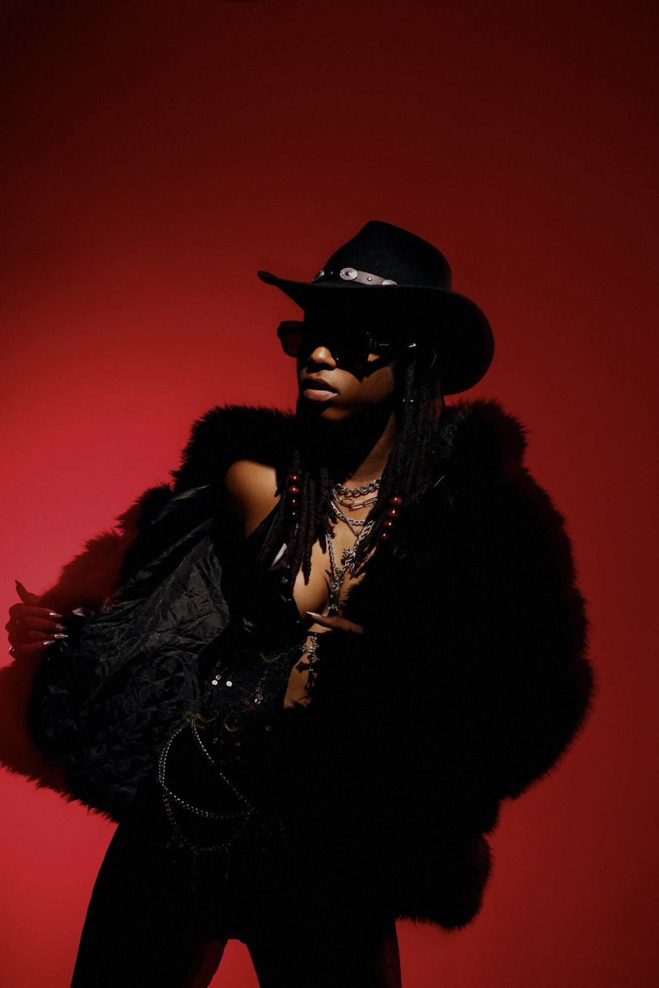 Person wearing a hat, sunglasses, and layered clothing against a red background.