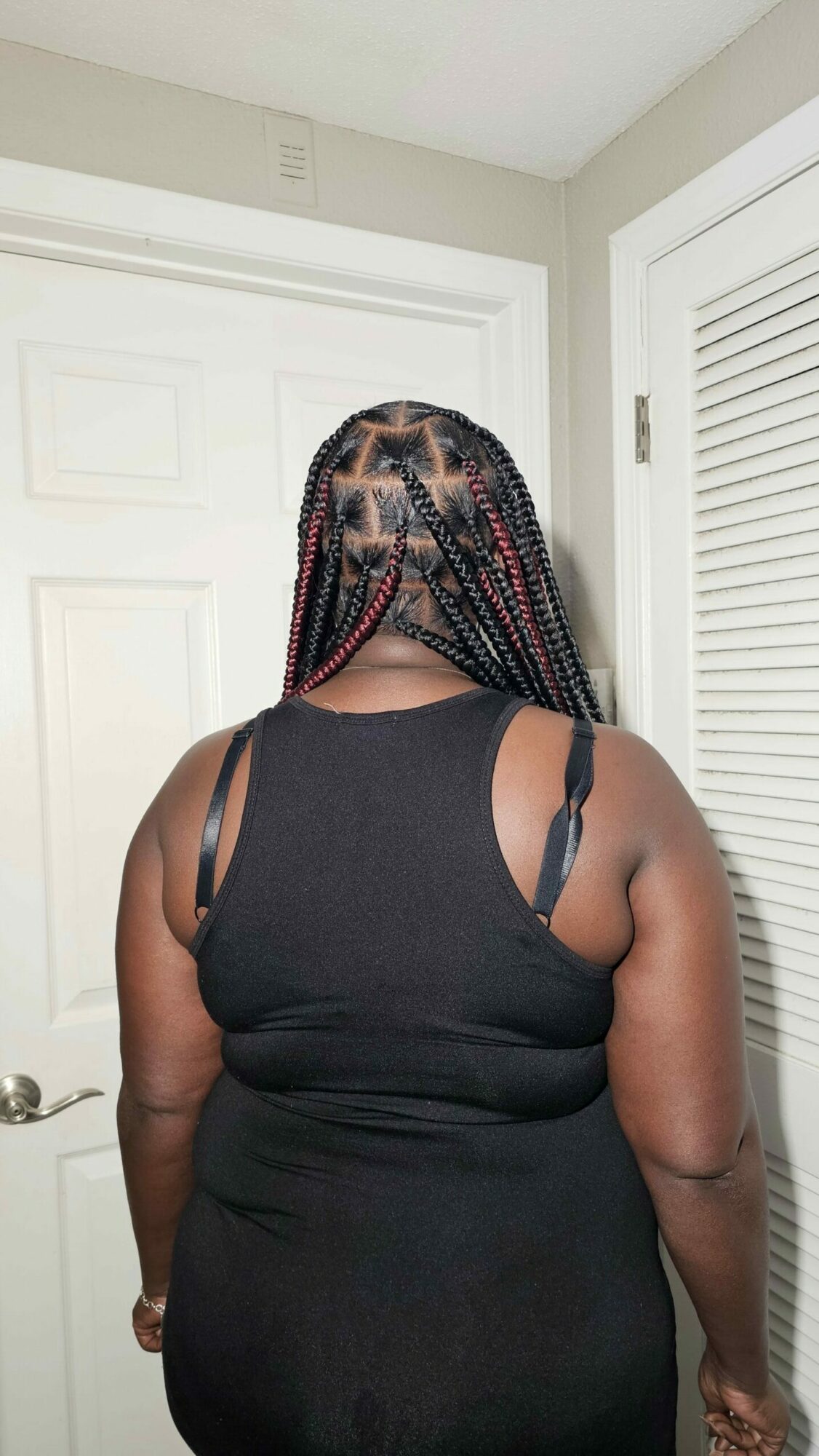 Person with braided hair wearing a black sleeveless top, standing indoors near a door.