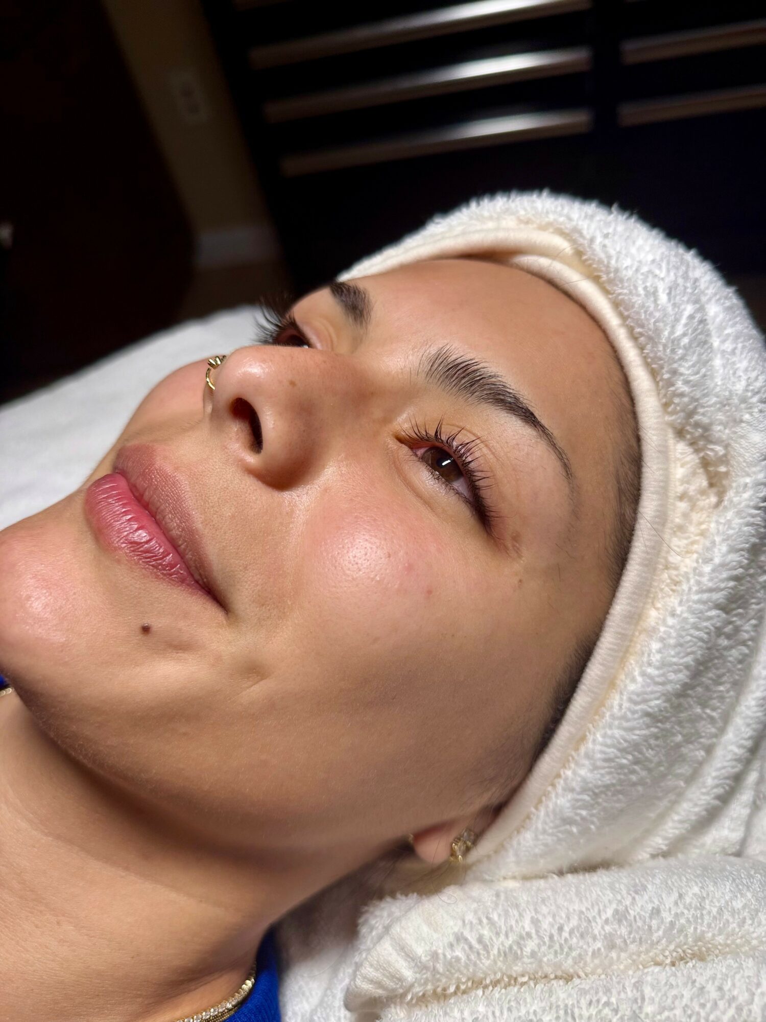 Close-up of a woman with a towel wrapped around her head, smiling softly, lying down with a relaxed expression.
