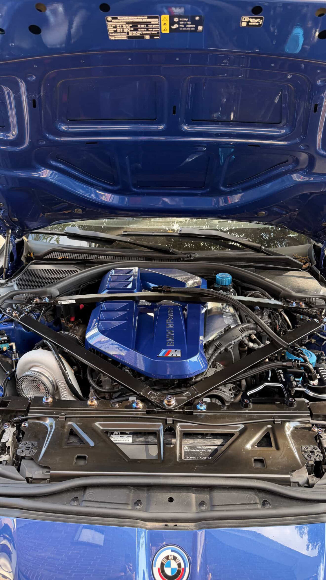 Car engine with blue cover and open hood, showing engine components and surrounding parts.