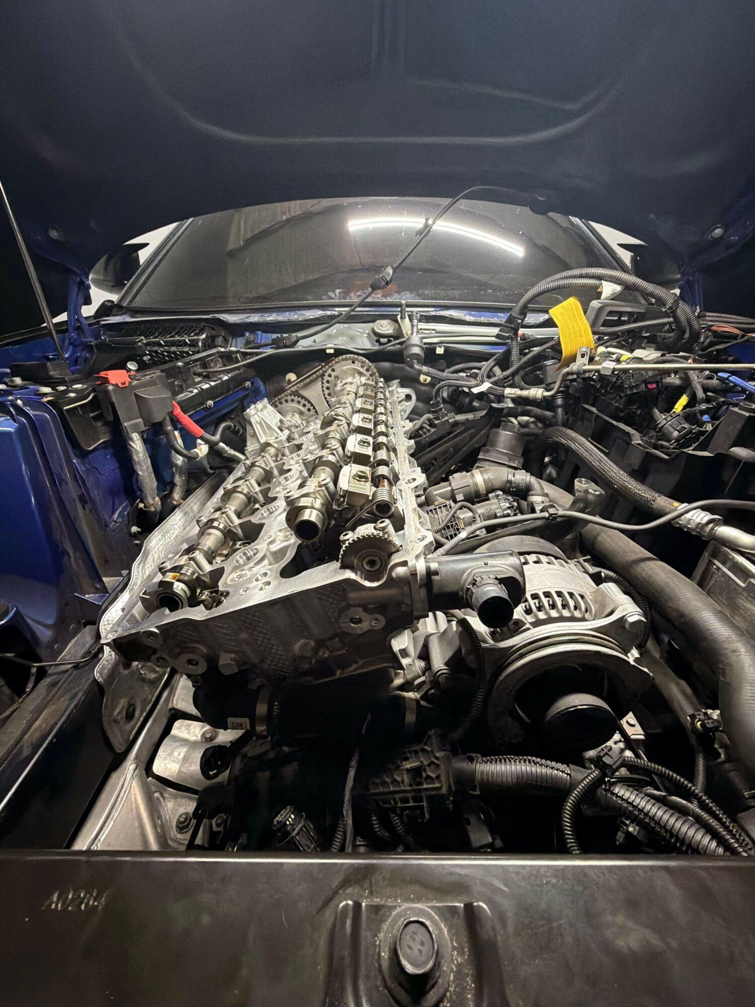 Car engine with visible components and wiring, viewed from the side, showing engine parts and surrounding area.