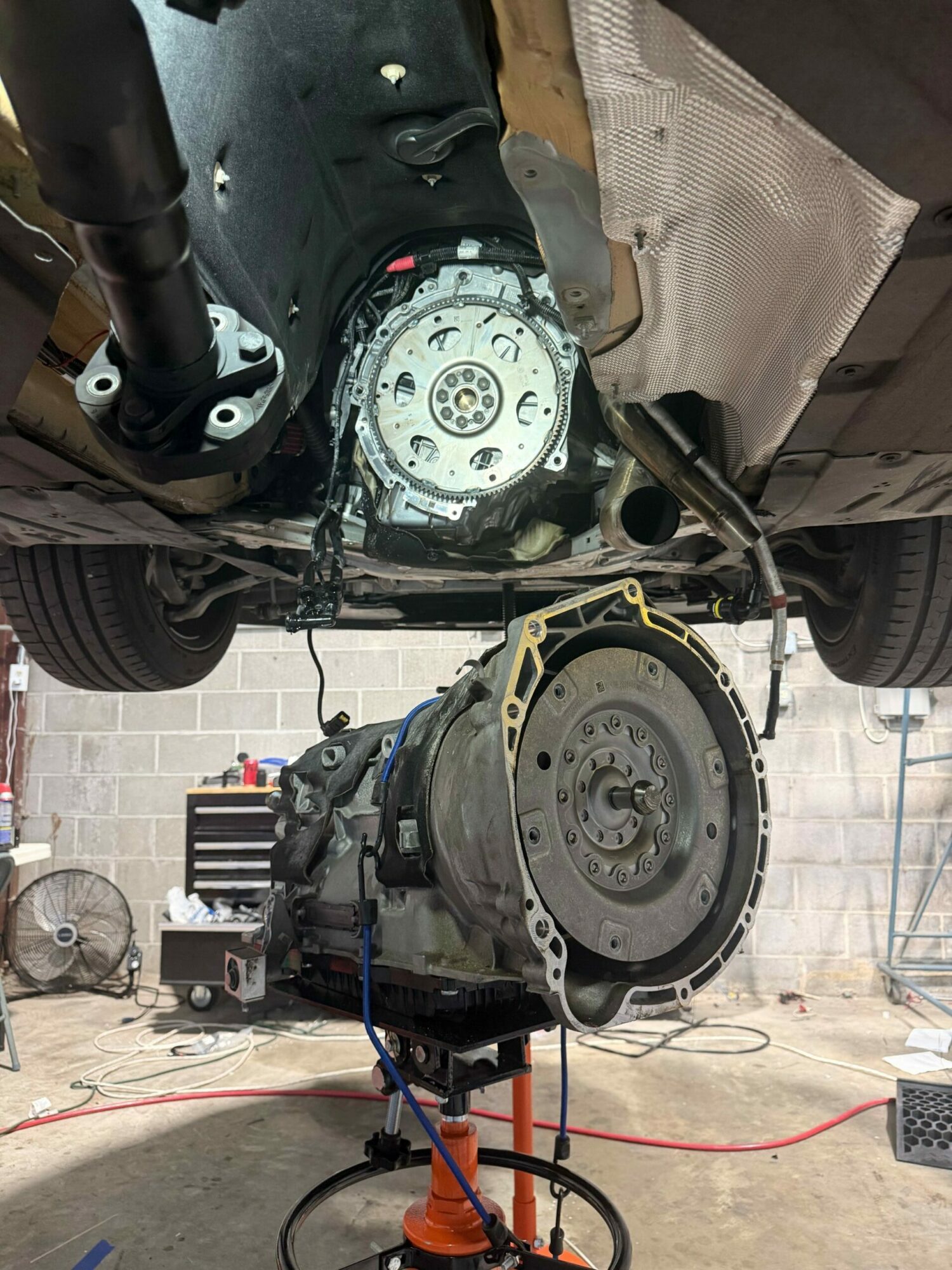 View of a disassembled vehicle engine with various parts and tools, including a motor and wiring, on a workshop floor.