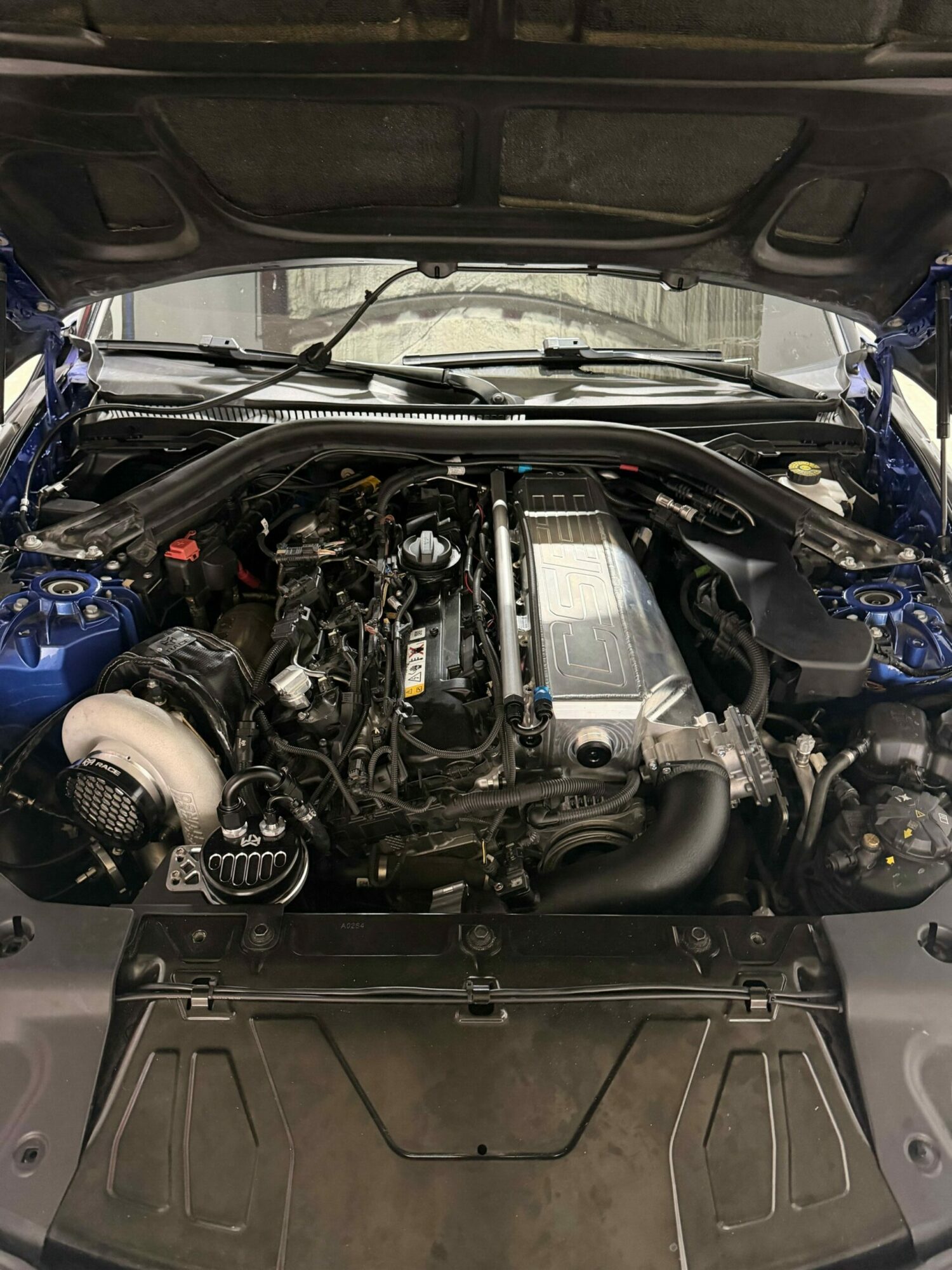 Car engine with various components, hoses, and a large turbocharger visible, viewed from above in a vehicle's engine bay.