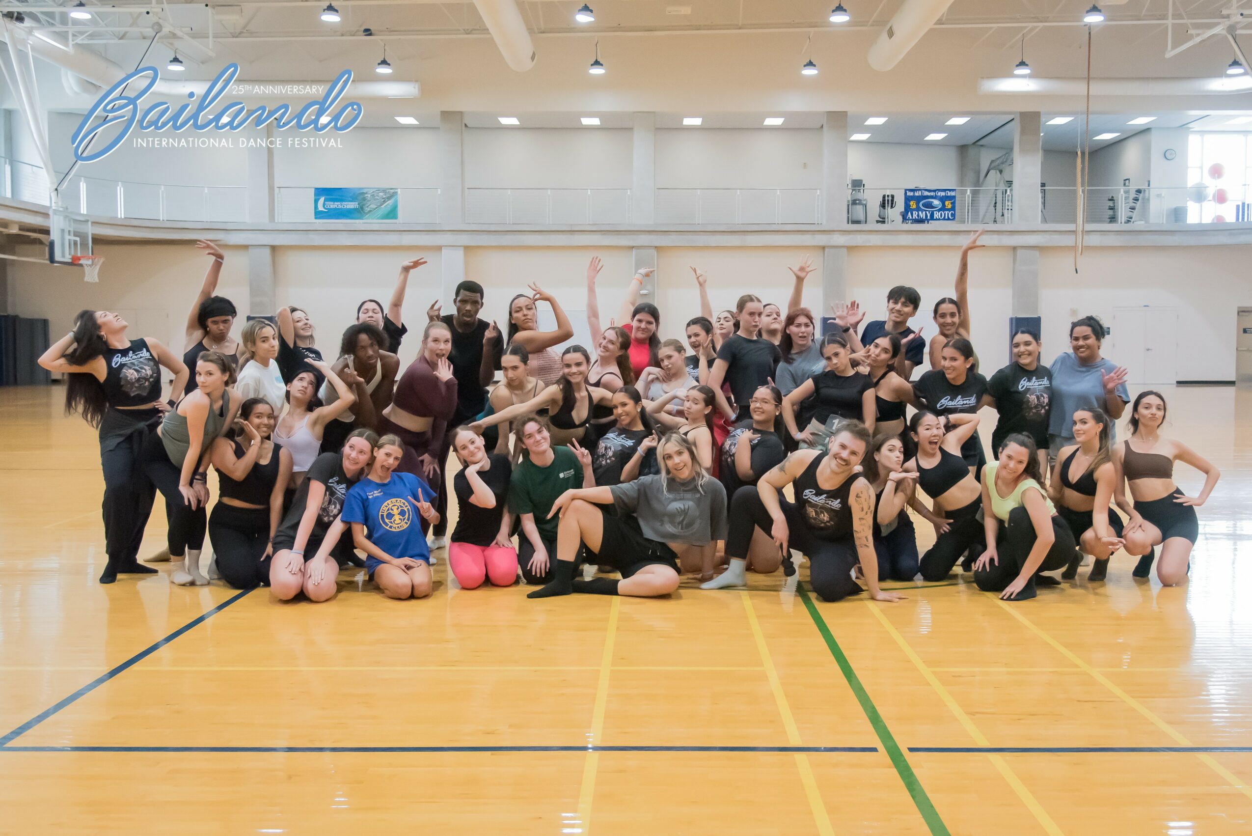 Group of people in dance studio, some sitting, some standing, raising arms, with a mirror and a sign that says 'Gailardo' in background.