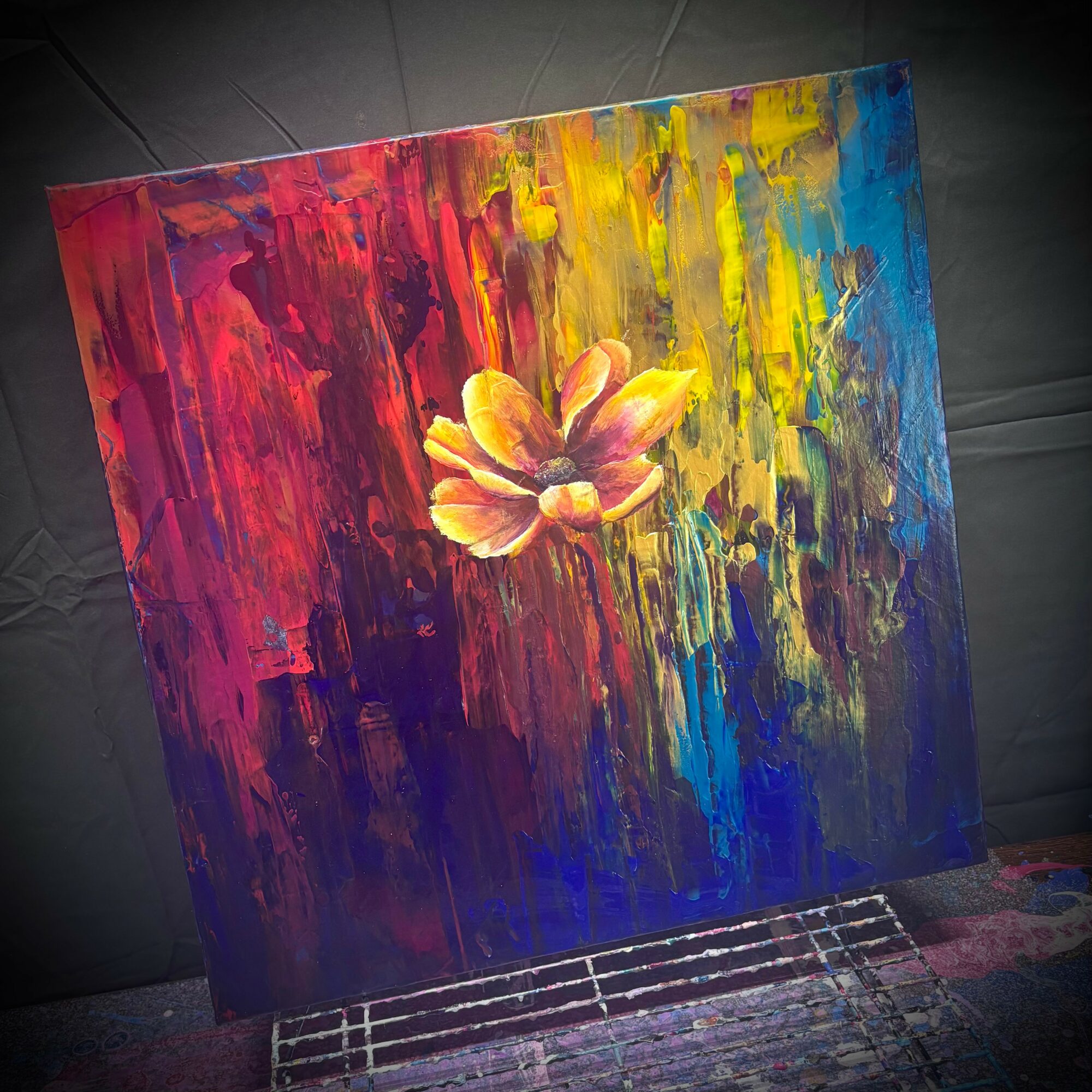 Colorful abstract painting of a flower with vibrant red, yellow, blue, and purple hues, on a textured background.