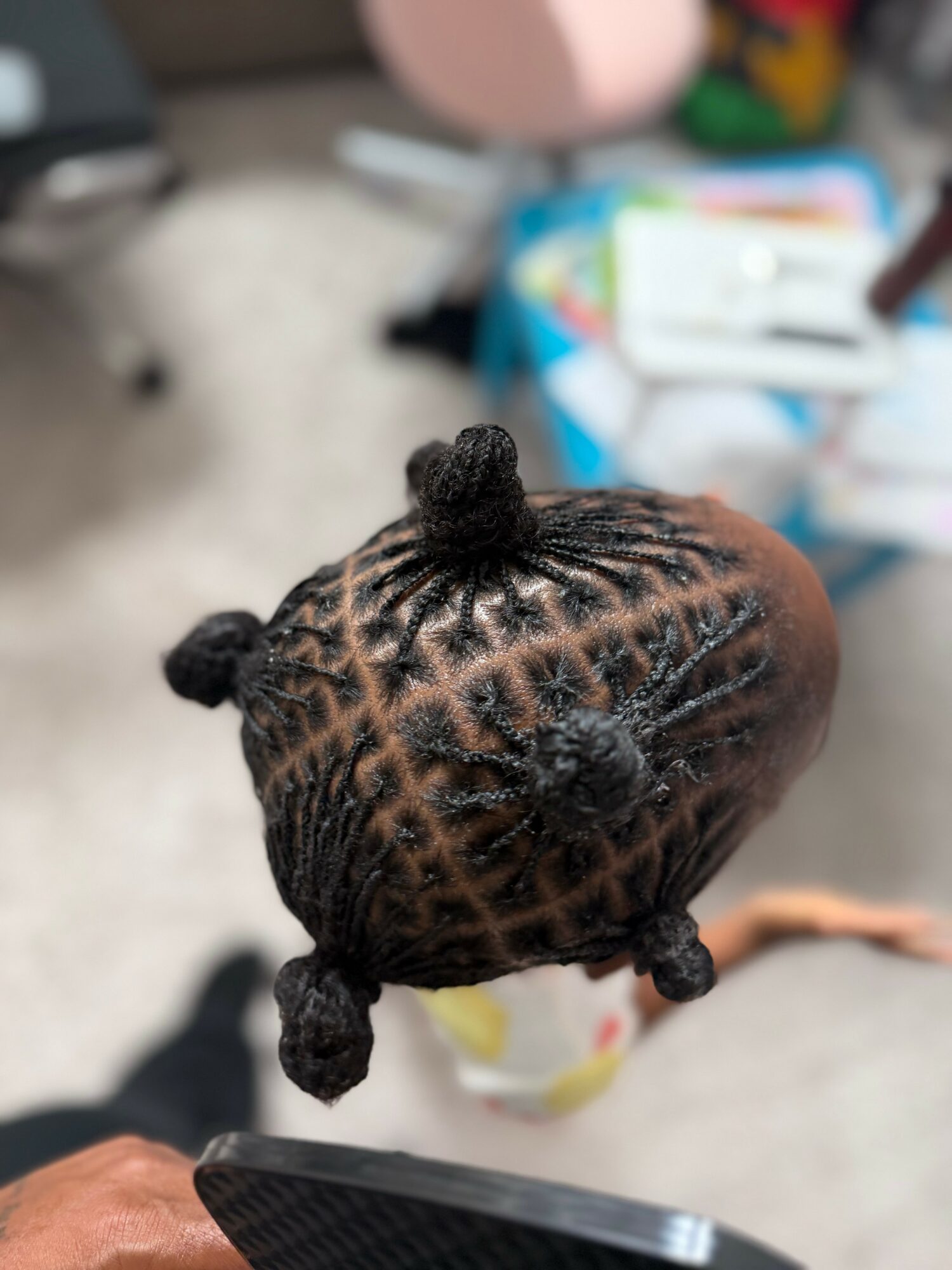 Top view of a child's braided hairstyle with small buns, on a person's head, indoors.