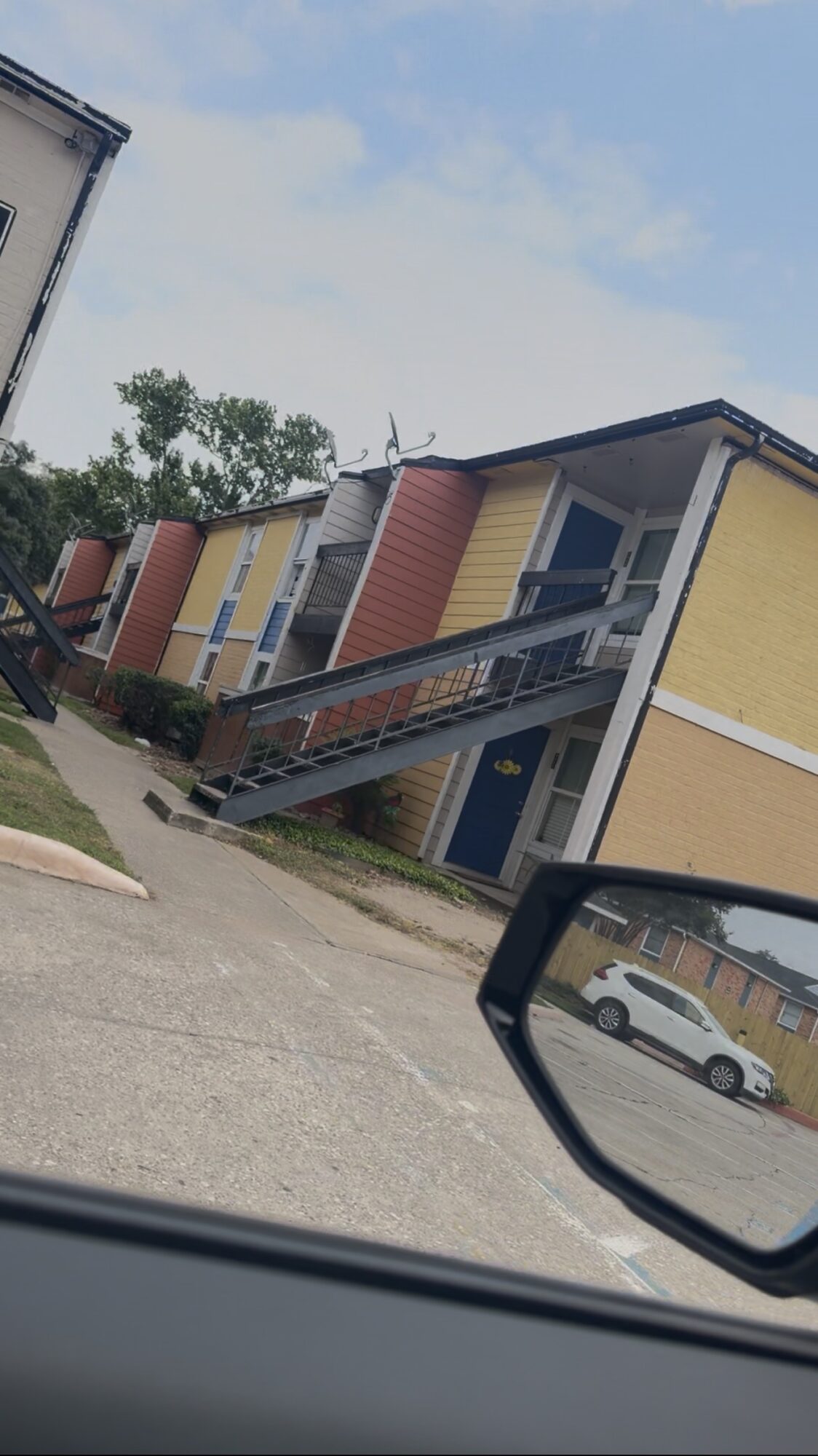 Colorful two-story building with yellow, red, and blue sections, viewed from a car window, with a parking lot and trees.