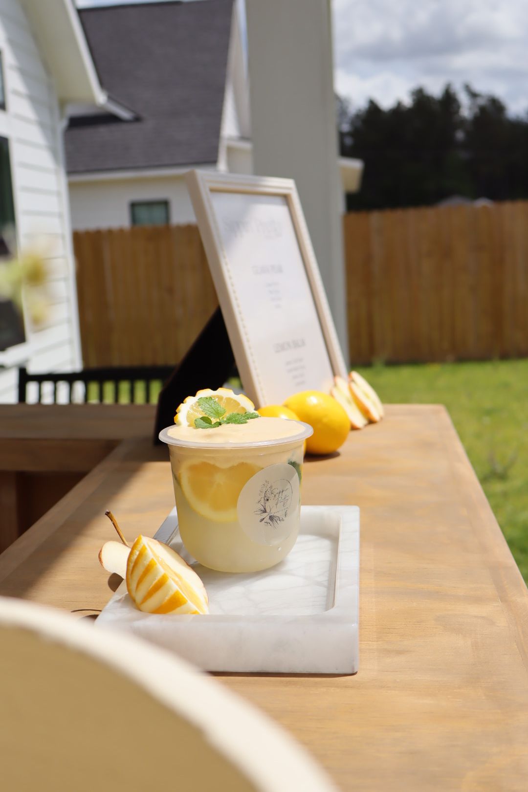 A yellow drink with a lemon slice and a straw on a wooden table, with a menu or sign in the background.
