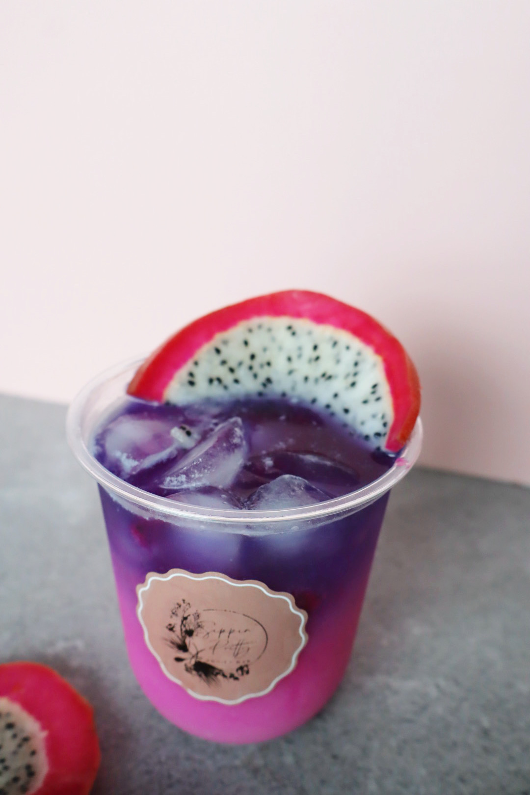 Cup with purple drink, ice, and a slice of dragon fruit on top, against a light background.