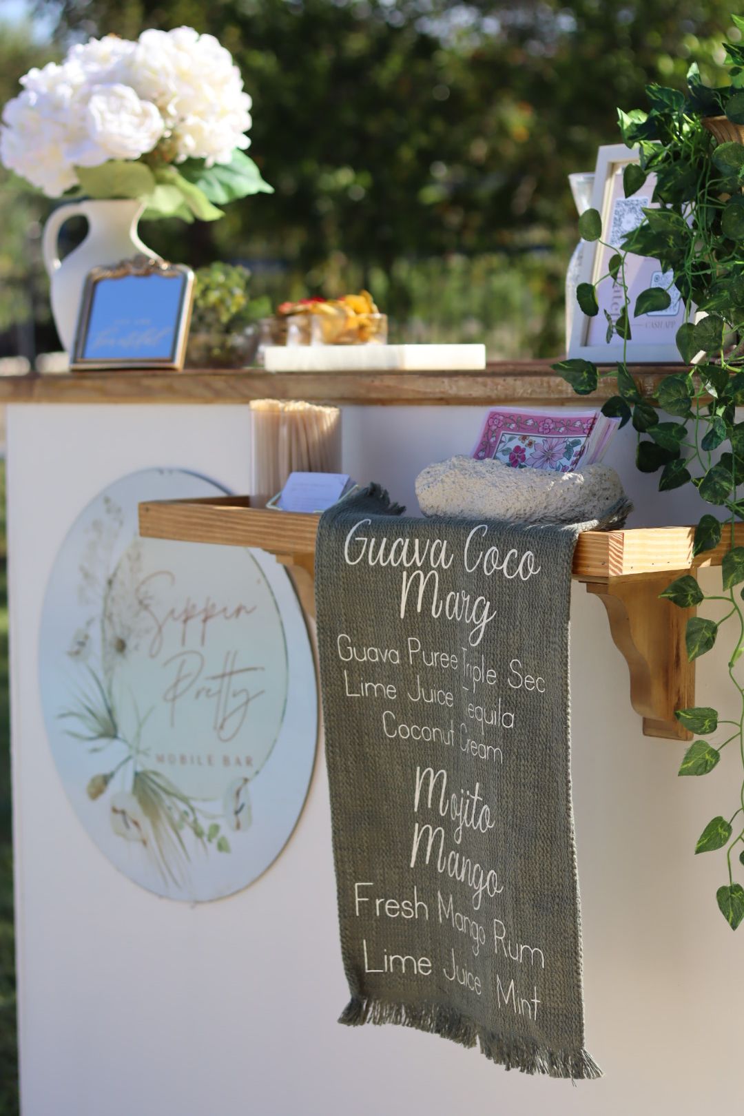 Decorative sign with text, a white hydrangea flower, a small framed picture, and a blue object outdoors.