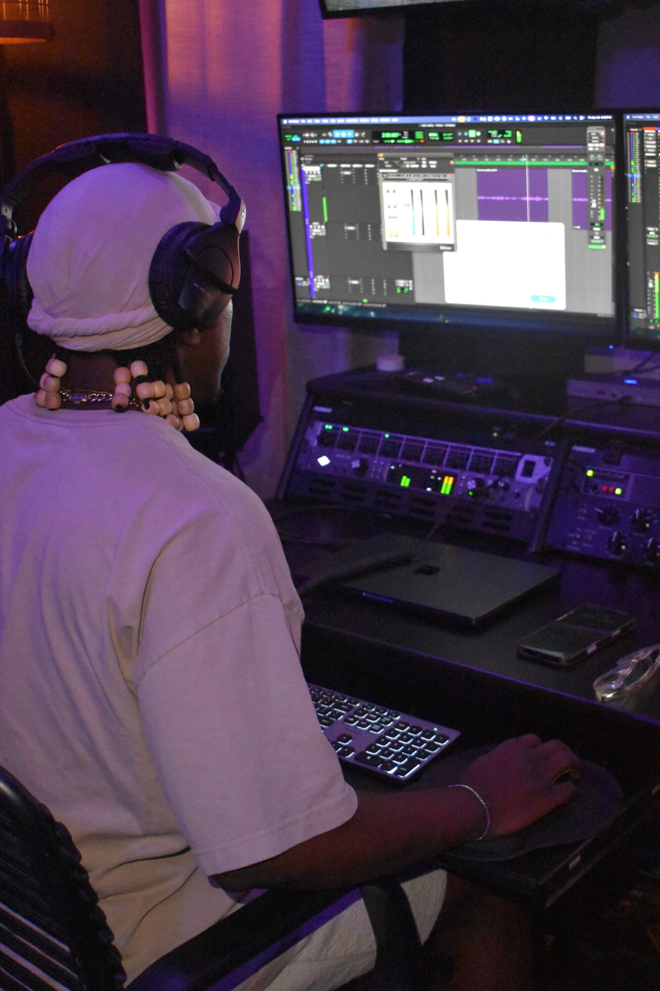 Person wearing headphones working on music production software at a computer station.