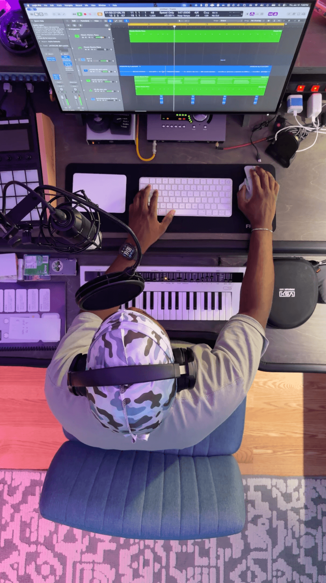 Person working at a music production setup with a computer, keyboard, and headphones, viewed from above.