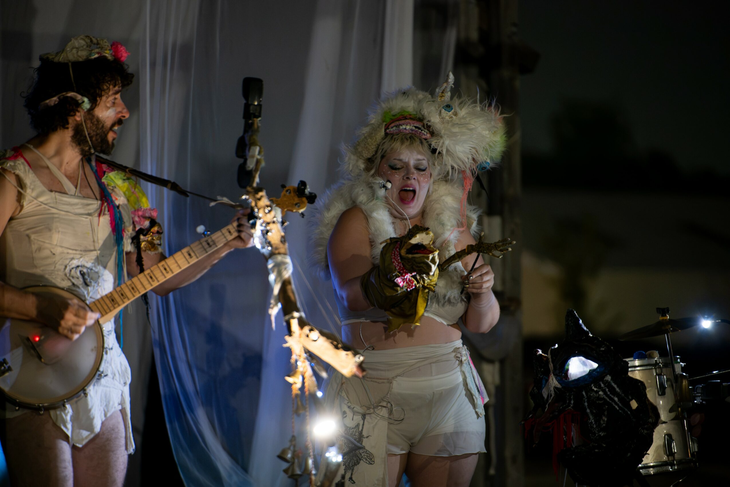 Two women perform on stage, one singing passionately and the other playing guitar, with stage lights and decorations.