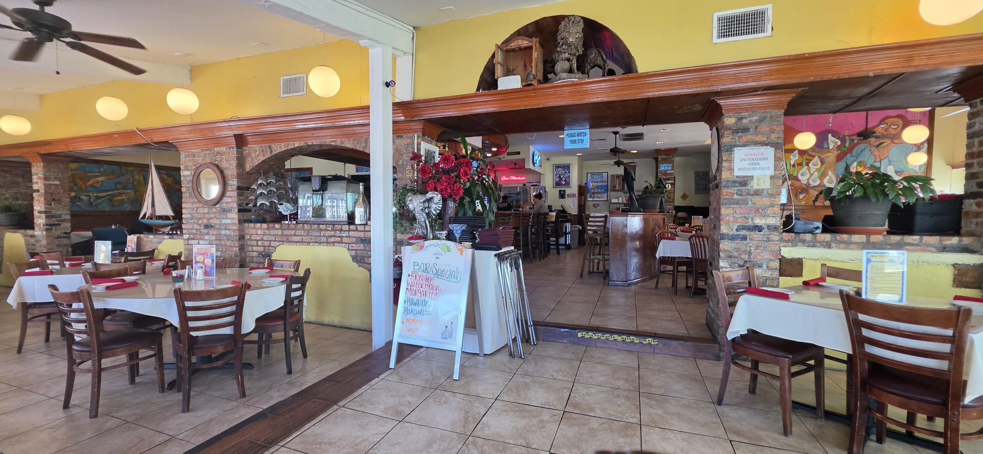 Restaurant interior with tables, chairs, and a bar area, decorated with flowers and colorful walls.