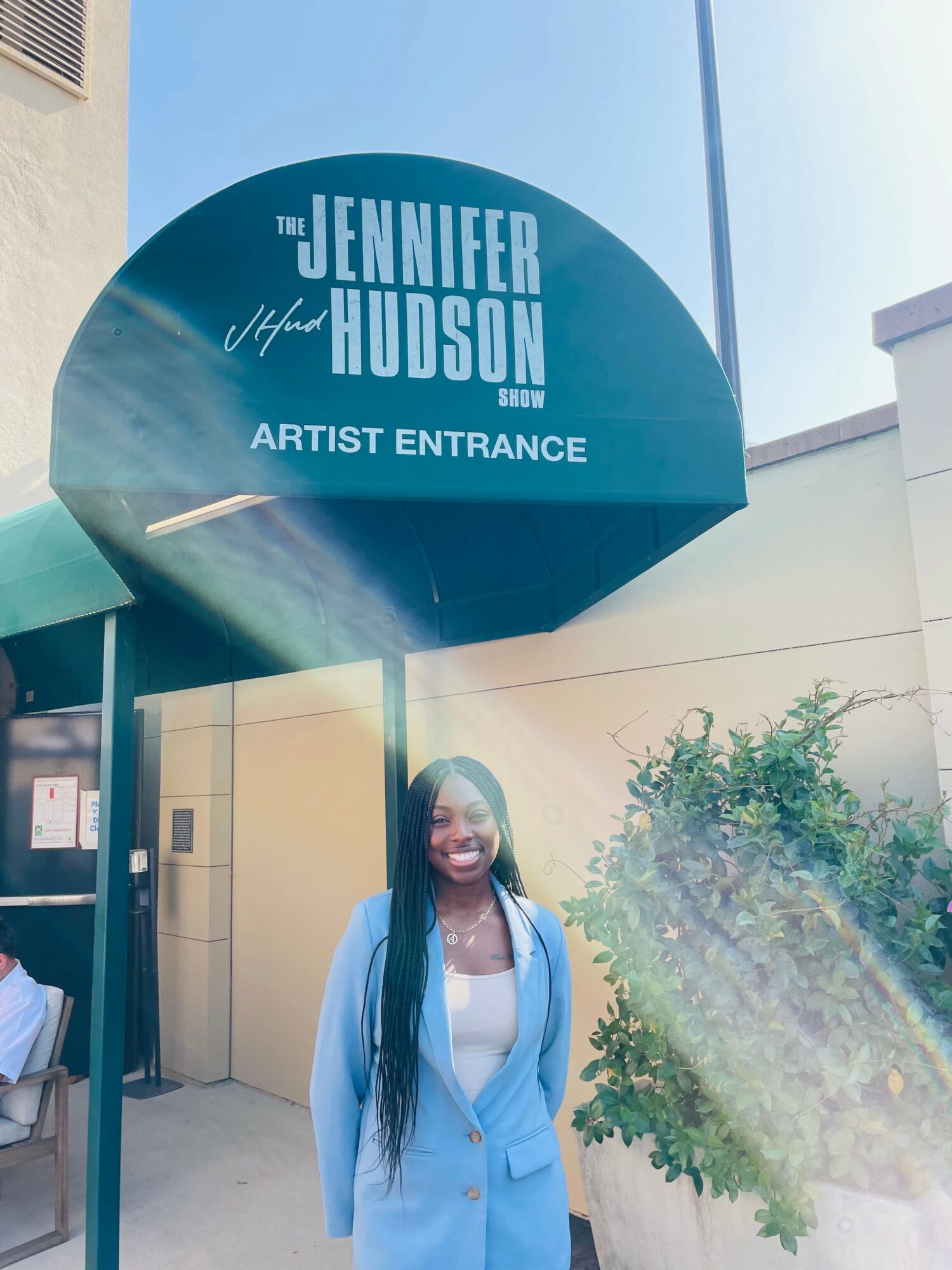 Woman with long hair smiling outside near a sign for Jennifer Hudson's artist entrance.