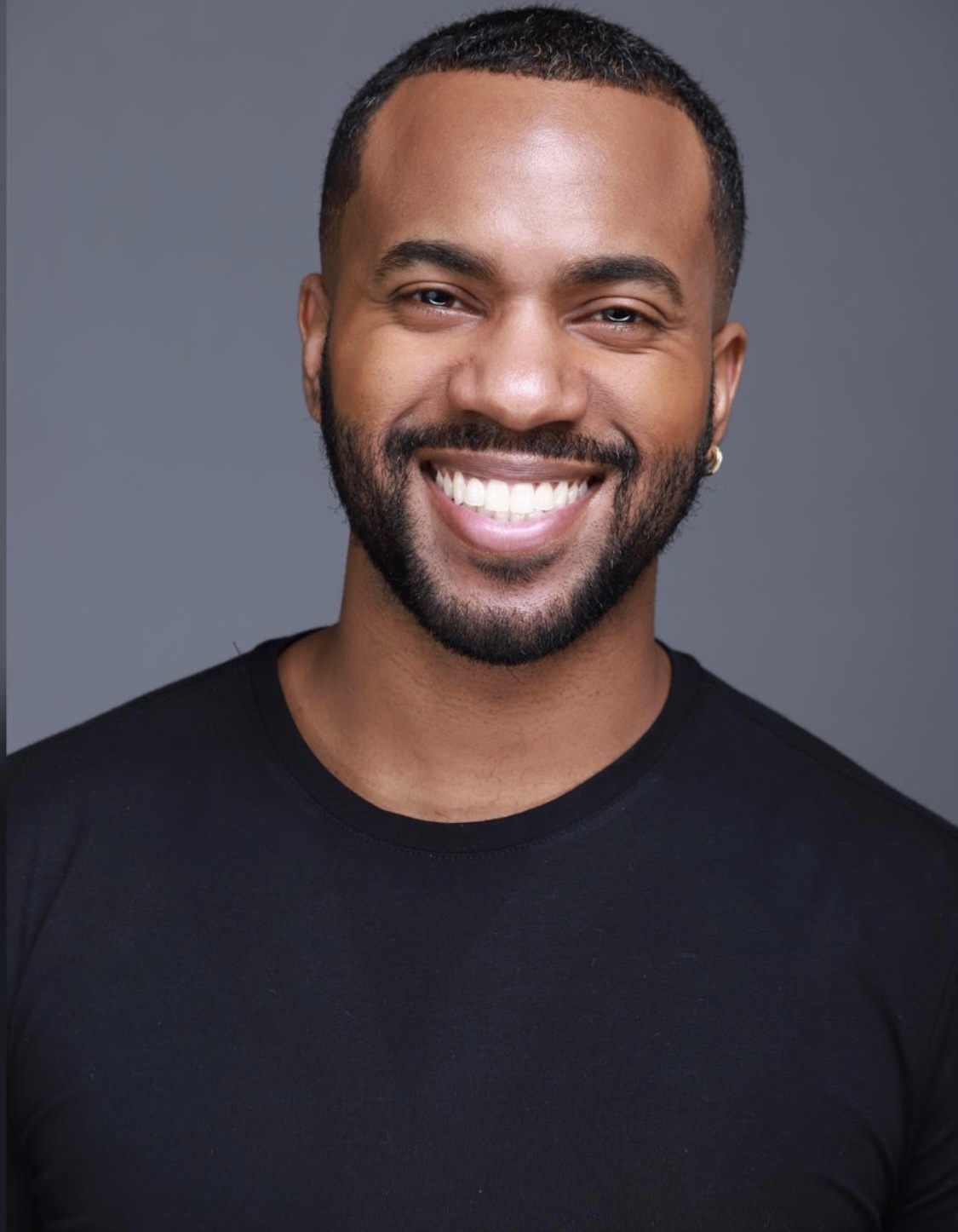 Smiling man with short hair and beard, wearing a black shirt, against a gray background.
