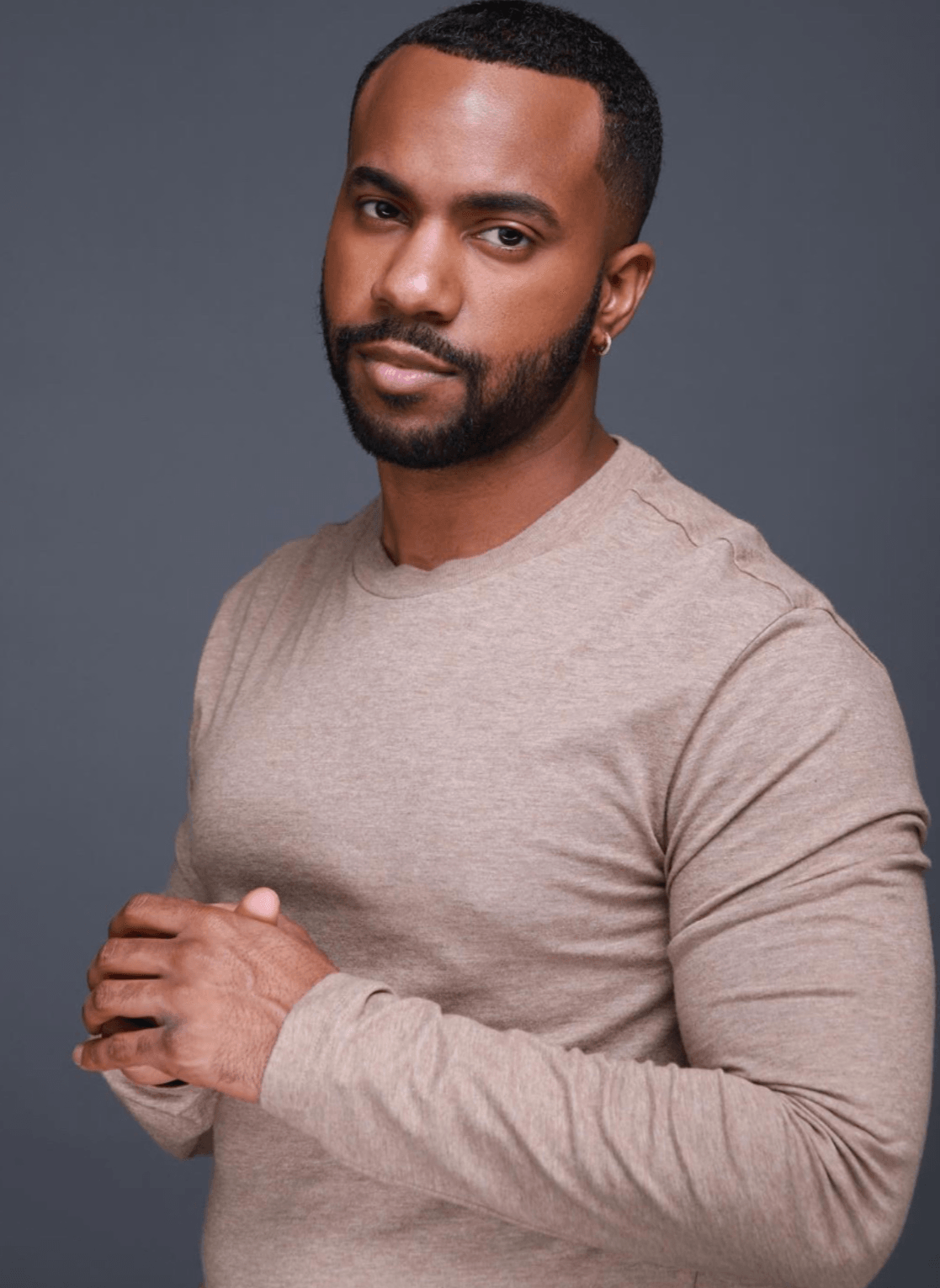 A man with a beard and short hair wearing a beige long-sleeve shirt, looking at the camera with a neutral expression.