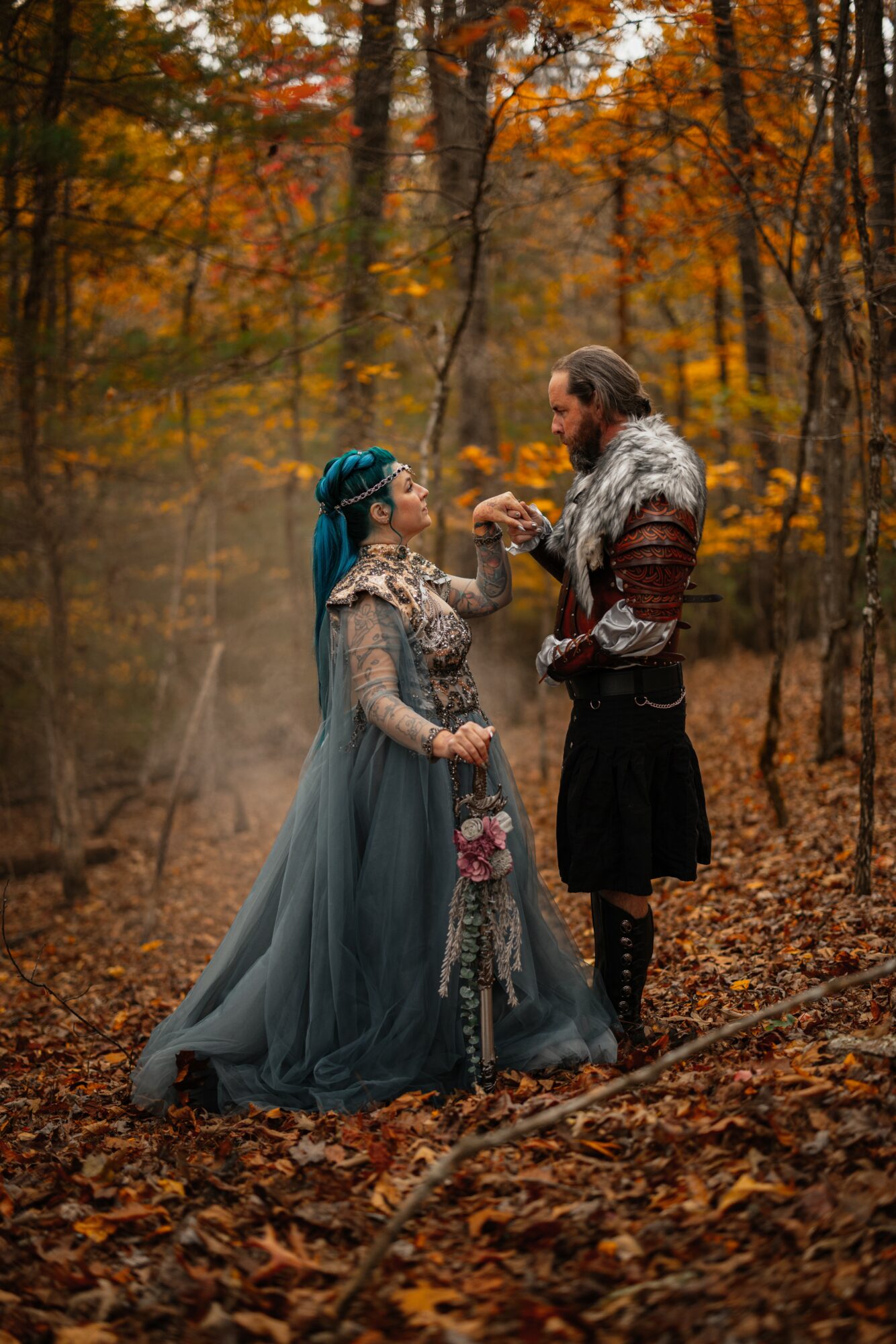 Two people in medieval costumes stand in an autumn forest, exchanging a small object, surrounded by fallen leaves.