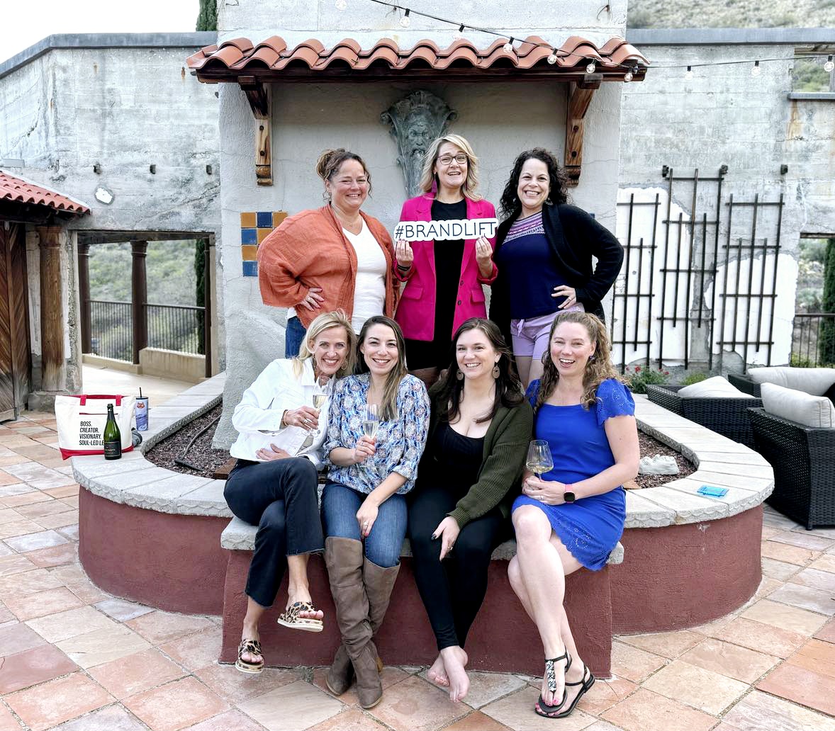 Six women pose in front of a fountain with a sign that reads '#BRANDLIFT'. They are smiling and dressed casually.