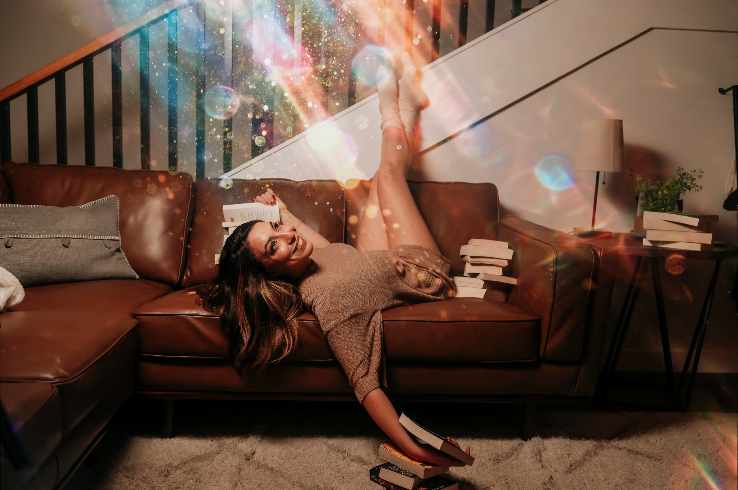 Woman lying on a sofa with books, colorful lights and a lamp in a living room, holding a book with her legs up.