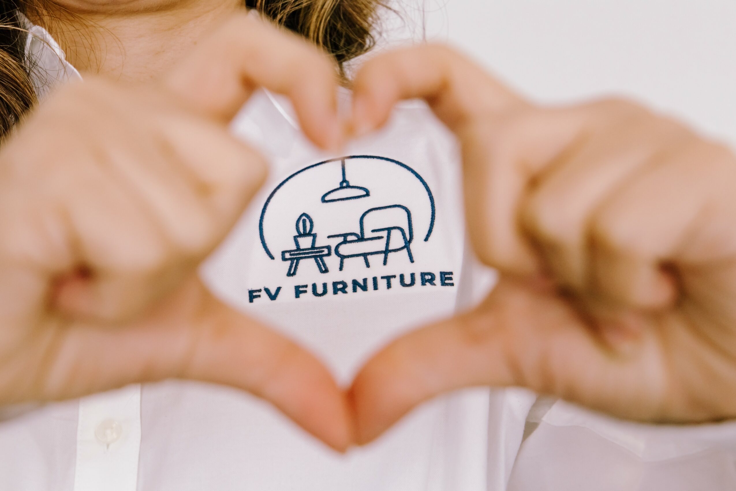 Person holding a round sticker with a furniture illustration and text, forming a heart shape with hands.