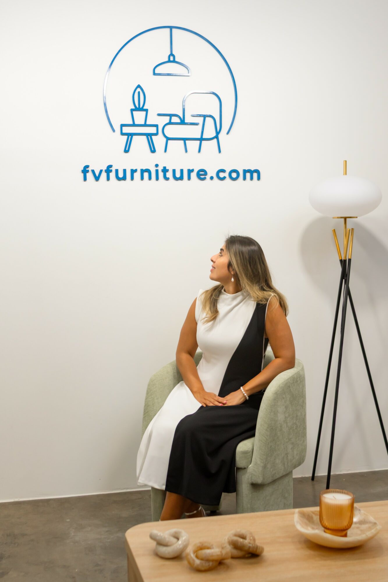 Woman sitting in a chair in a furniture store, with a logo and website on the wall behind her.