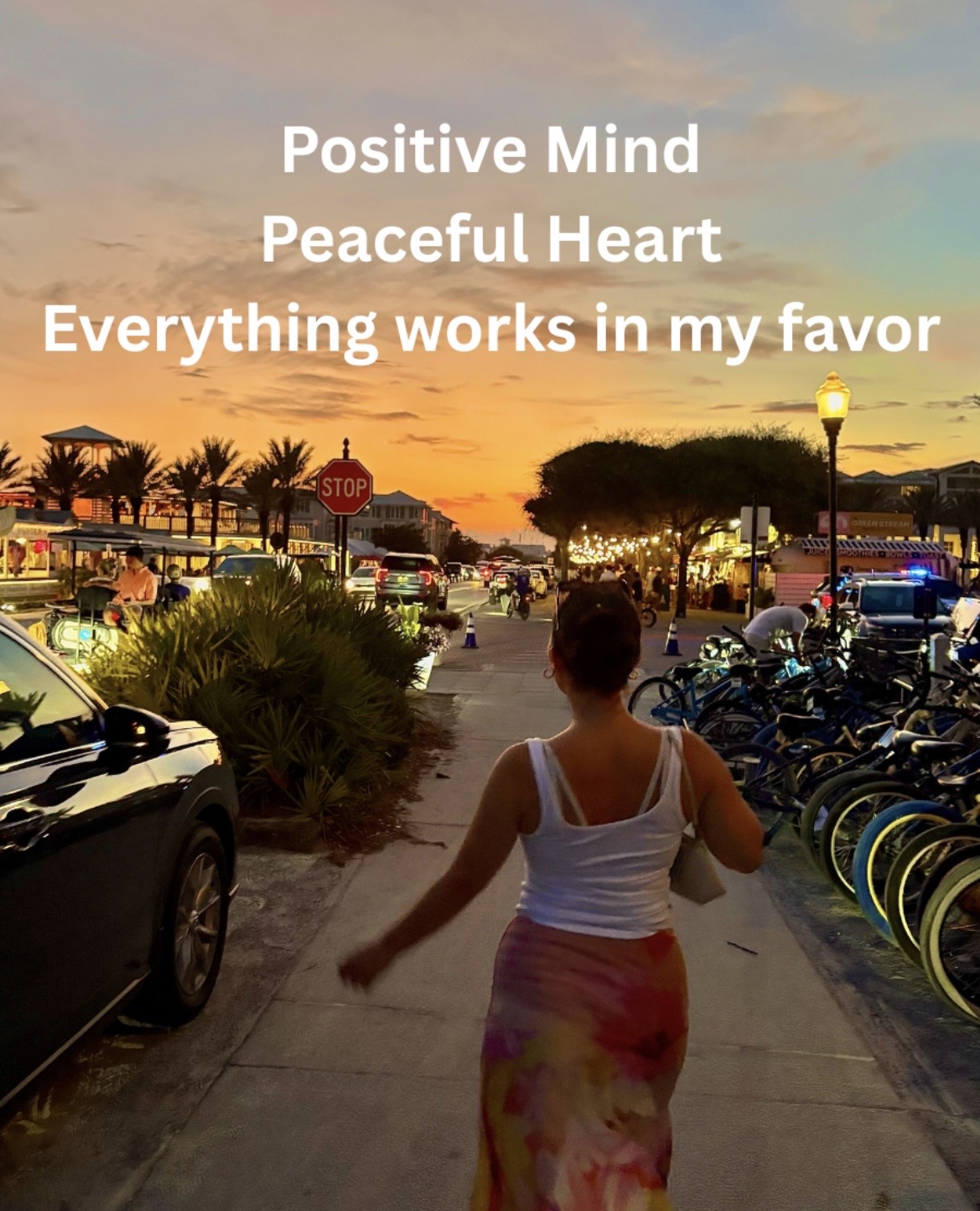 Person walking on sidewalk with parked cars and bicycles, sunset sky, trees, and streetlights in background, positive message overlay.