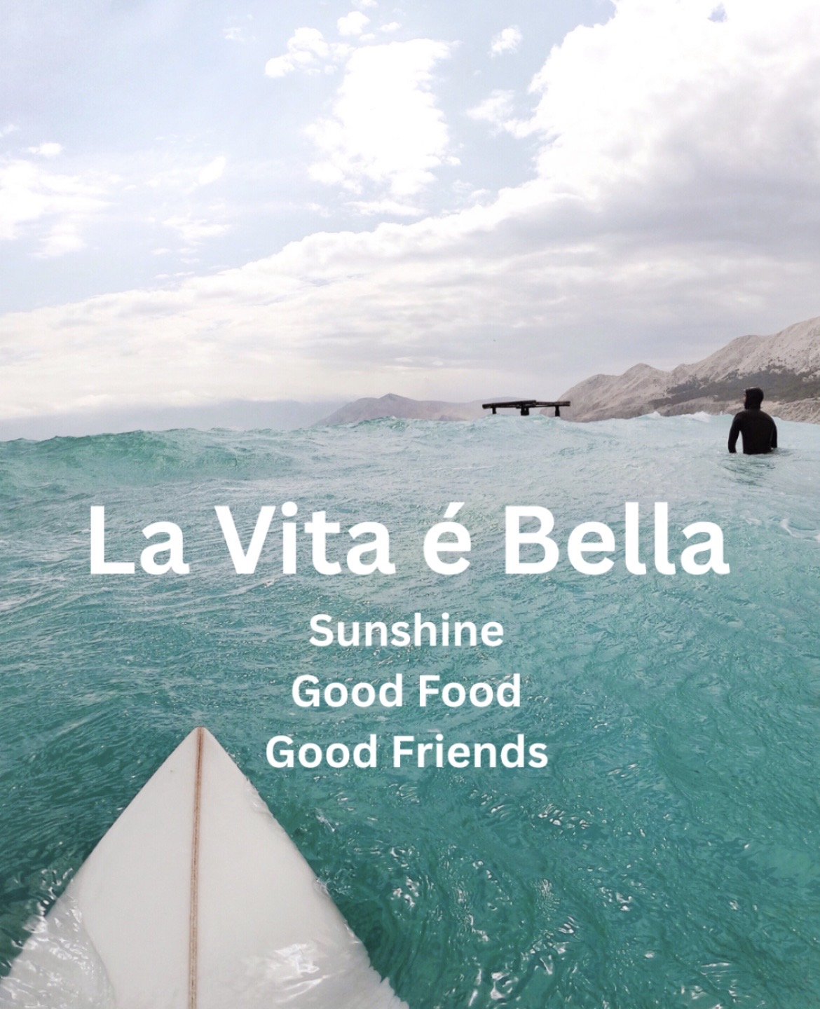 View from a boat on the ocean with a person in the water, mountains in the background, and a cloudy sky.
