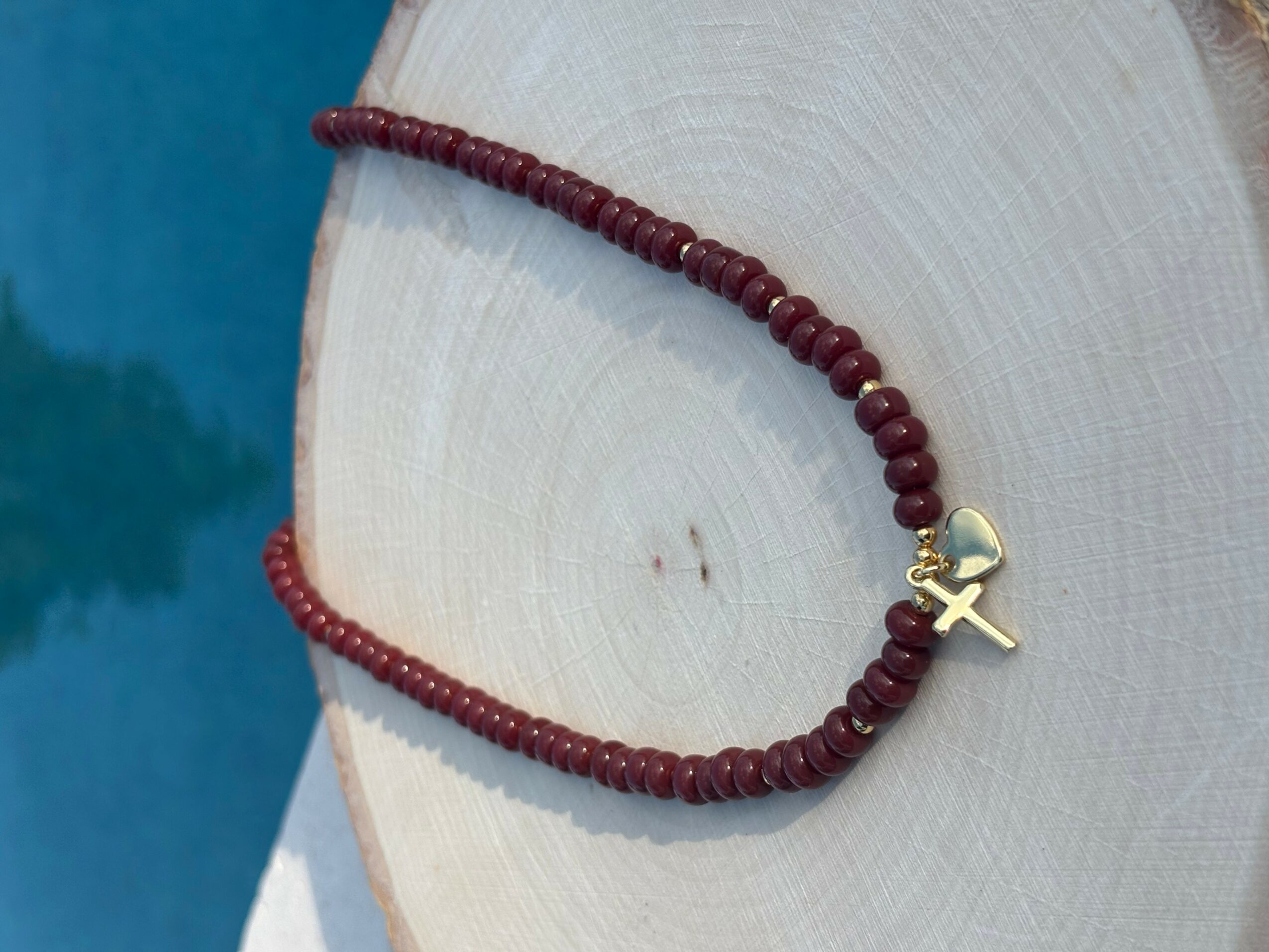 Red beaded necklace with a gold cross pendant displayed on a white circular surface.