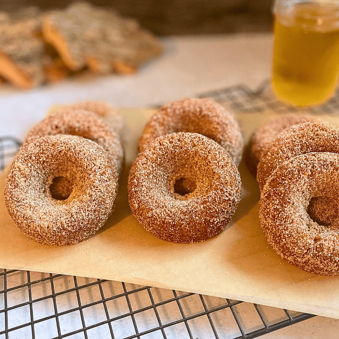 Six sugar-coated donuts on parchment paper with a glass of beer in the background.
