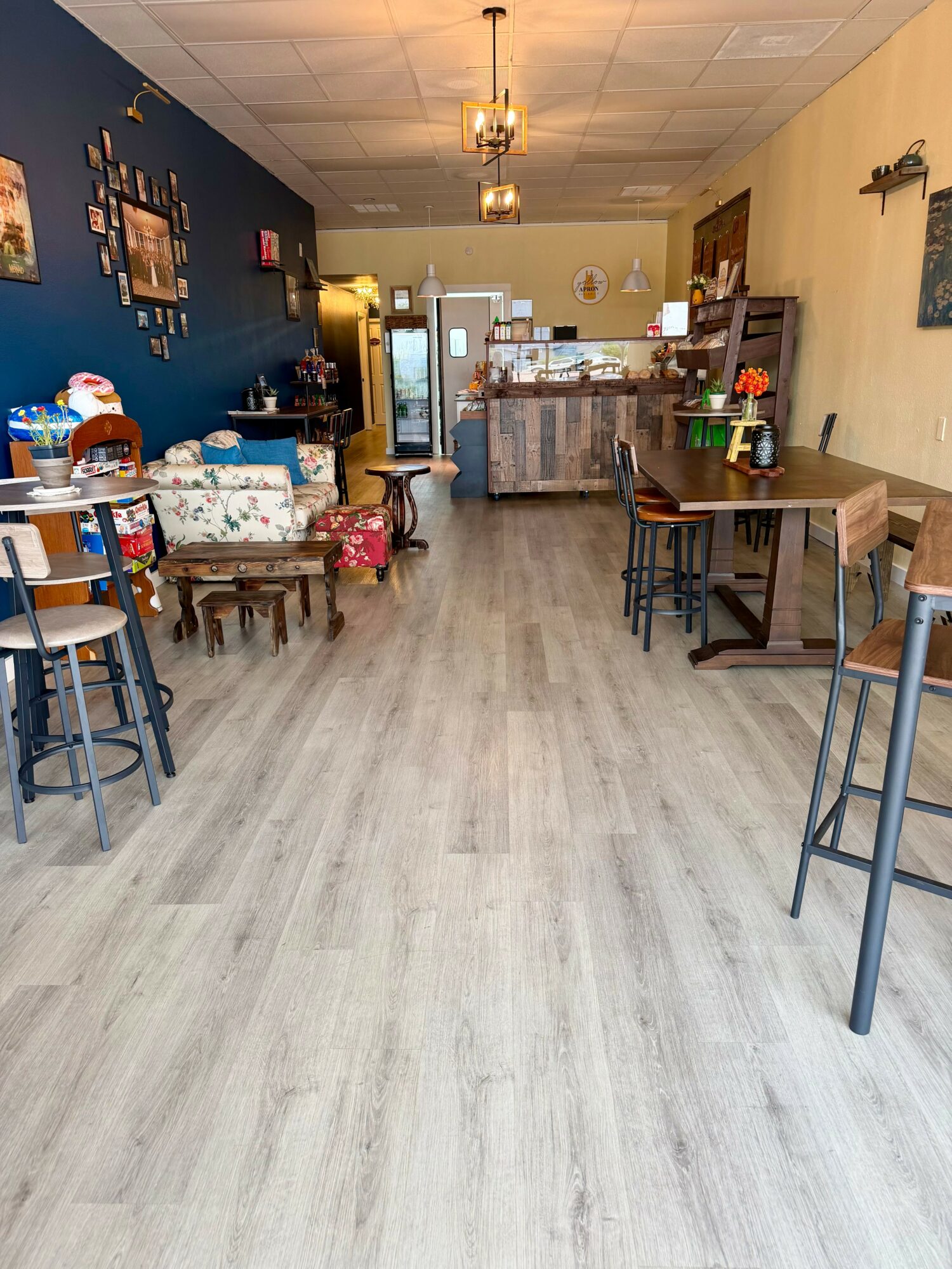 Empty cafe with tables, chairs, and a counter in the background, wooden flooring, and a chandelier ceiling light.