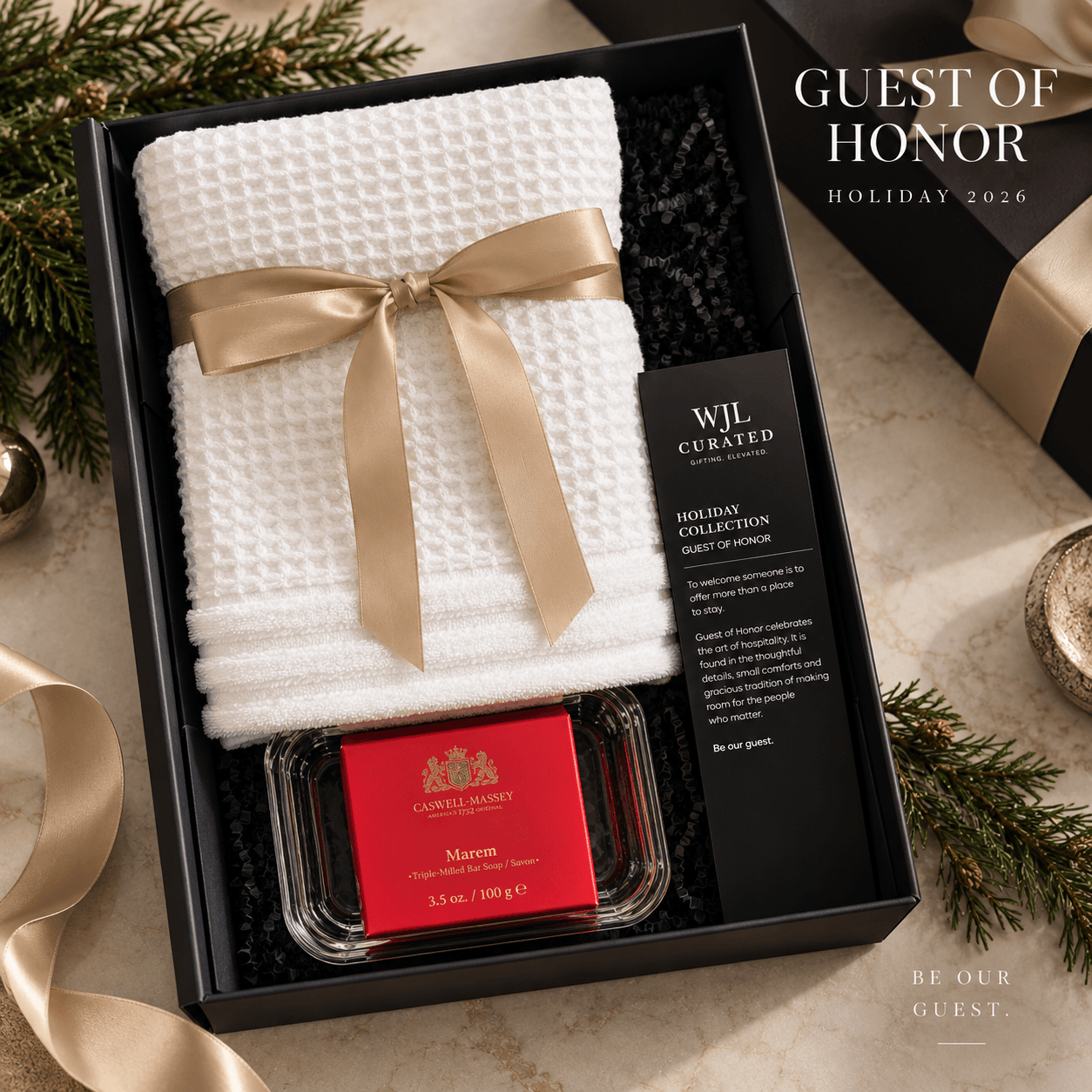 Gift set with white towel, gold ribbon, red soap, and black box, decorated with pine branches and gold ribbon, for holiday 2026.