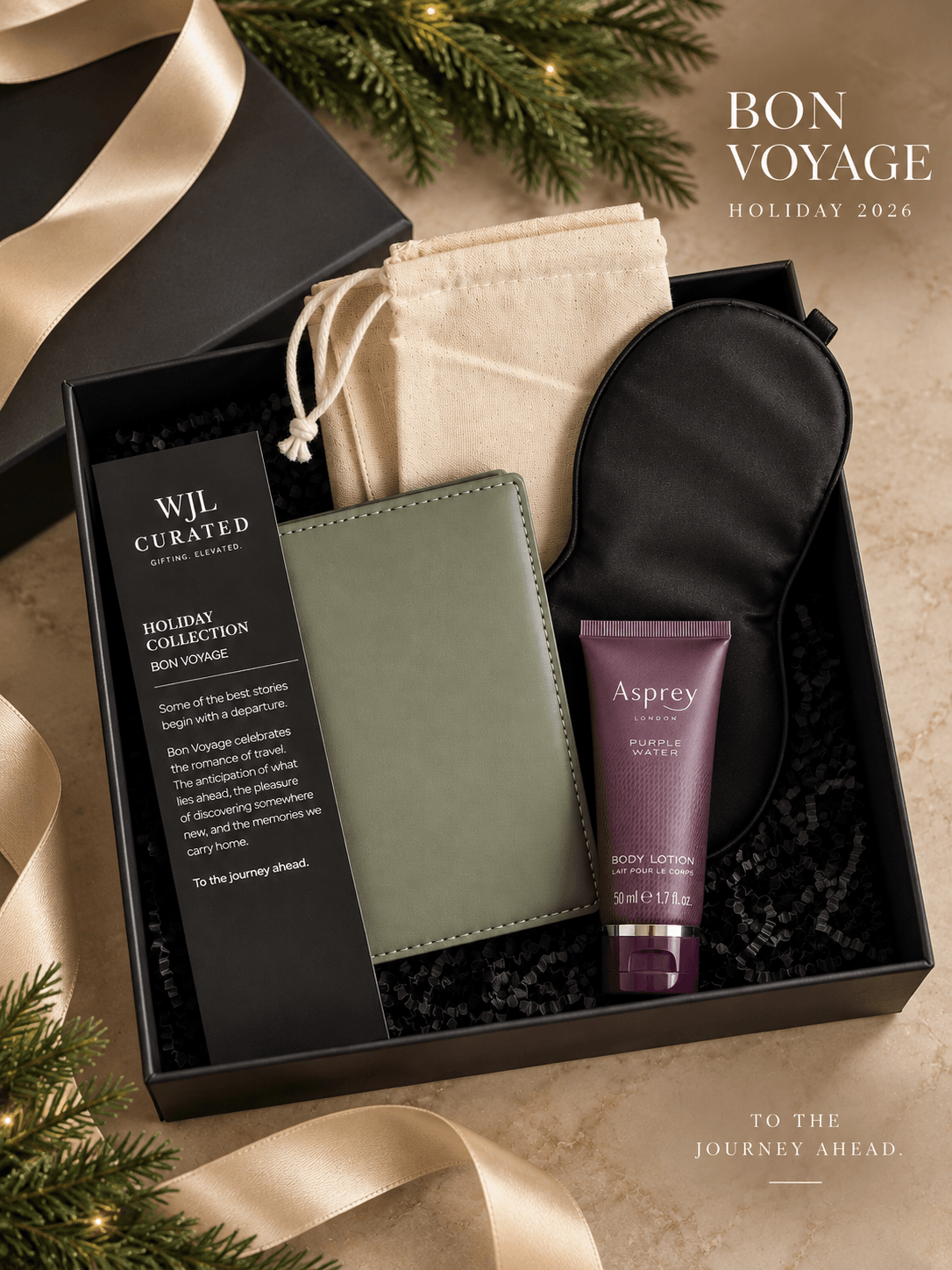 Gift box with a black pouch, green notebook, cream drawstring bag, and purple tube, surrounded by greenery and ribbon.