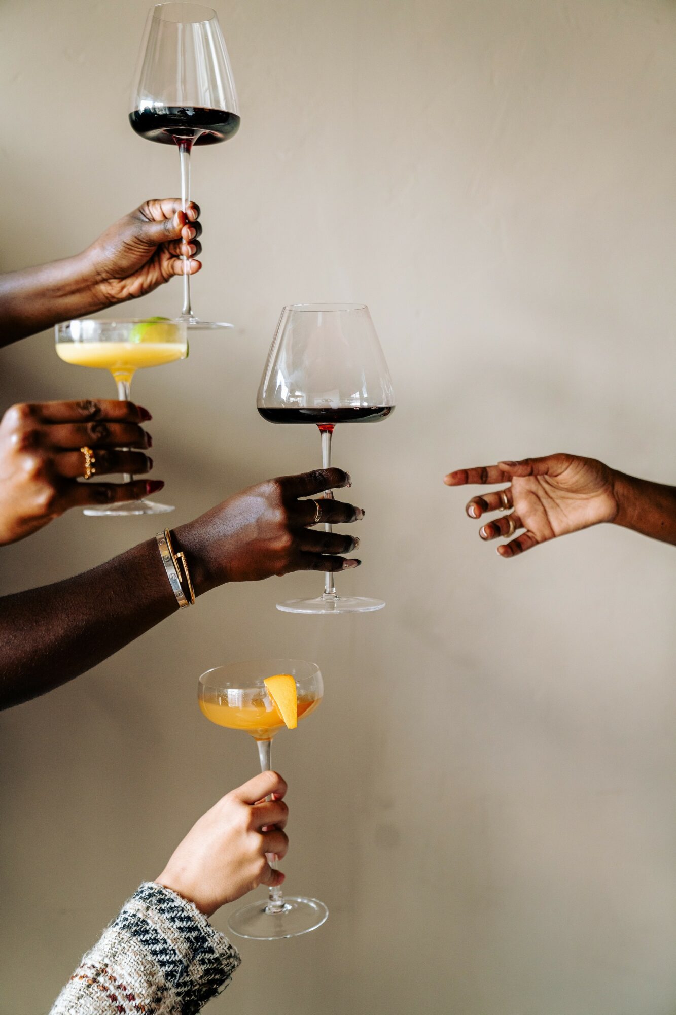 Multiple hands holding wine glasses and a plate with lemon slices, with a plain background.