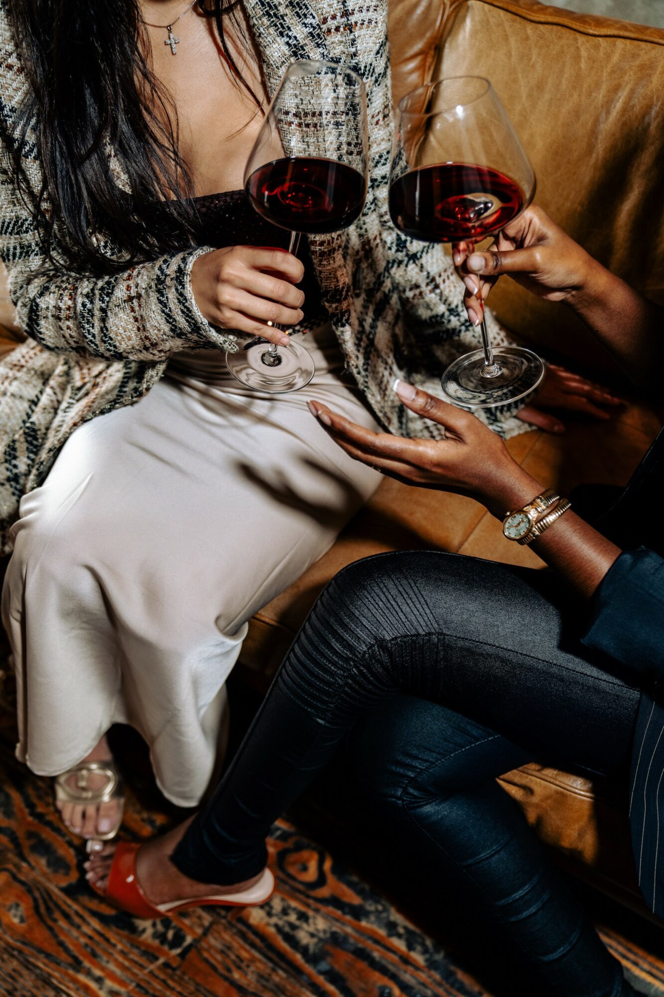Two people holding glasses of red wine, sitting close together on a sofa, with one person's hand on the other's lap.