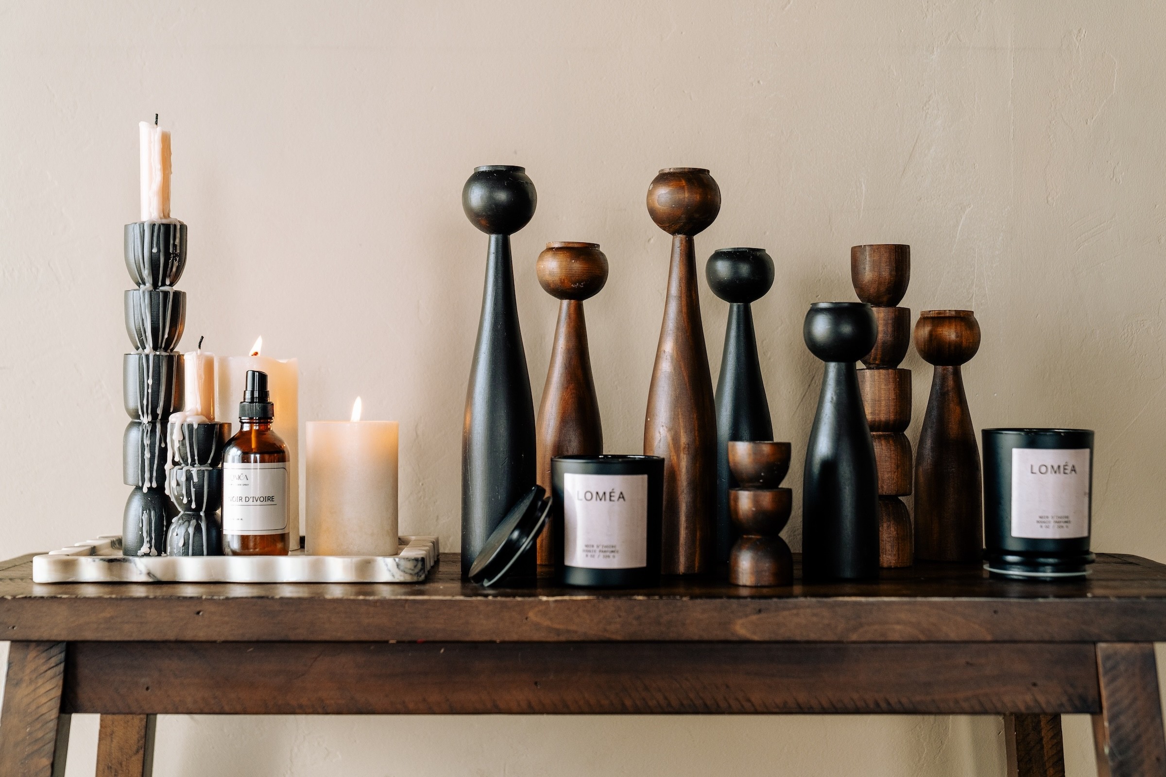 Decorative candles and wooden objects on a dark wooden table against a plain wall.