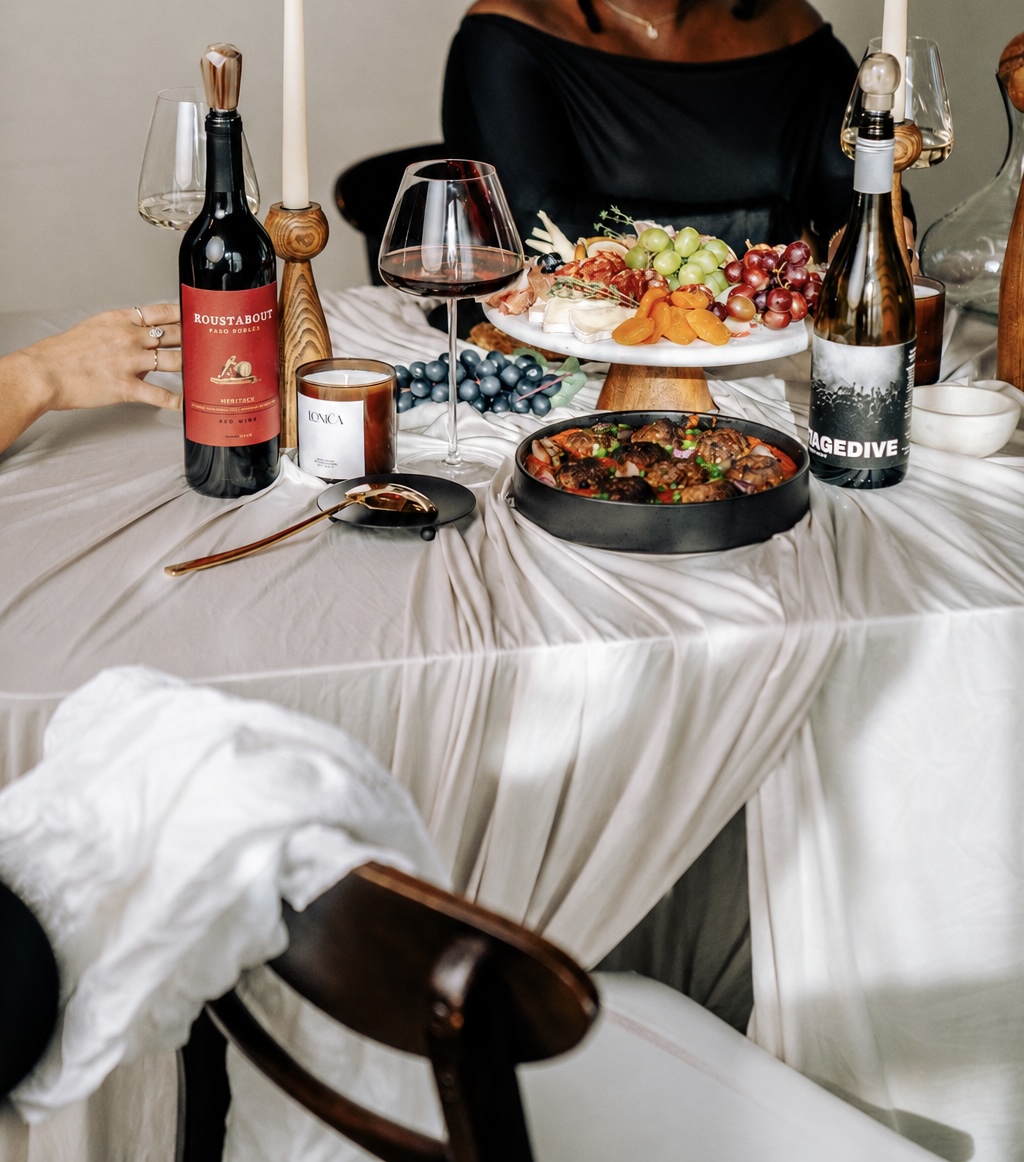 People dining with food, wine, and drinks on a table covered with a white tablecloth.