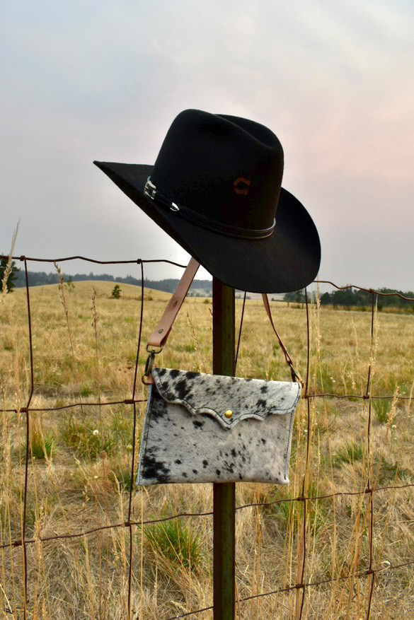 Black hat hanging on a fence post with a bag below, in a grassy field with a cloudy sky.