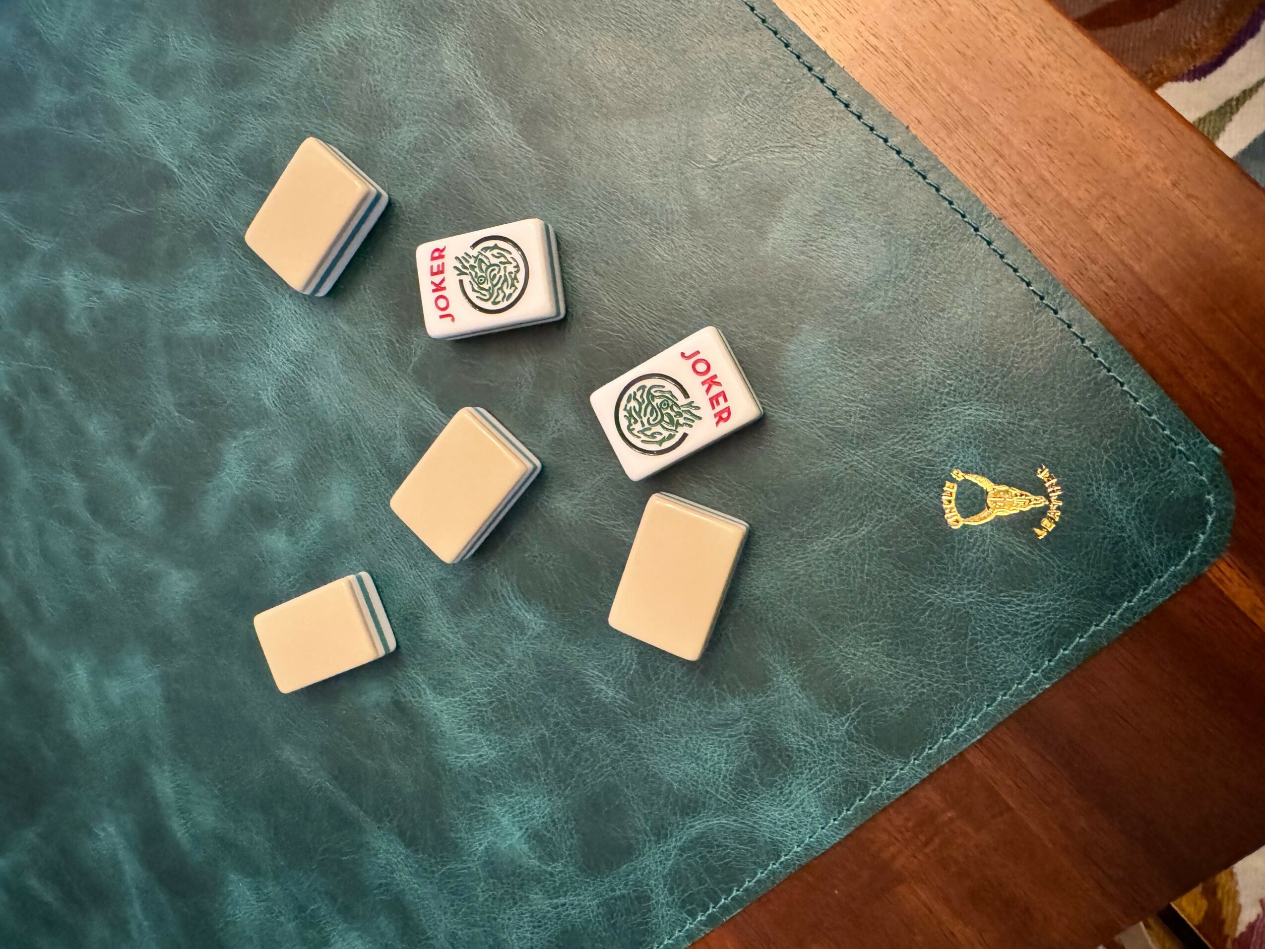 Six rectangular objects and two matchboxes on a teal surface with a gold anchor emblem, viewed from above.