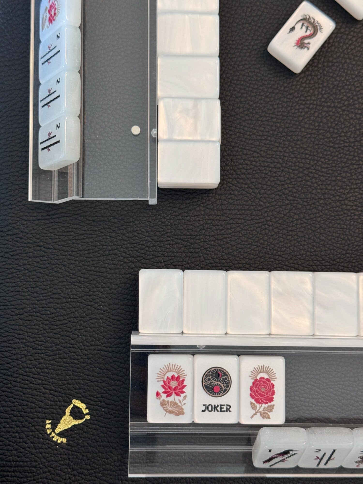 Mahjong tiles and a tile rack on a black surface, with a joker tile and a small decorative object nearby.