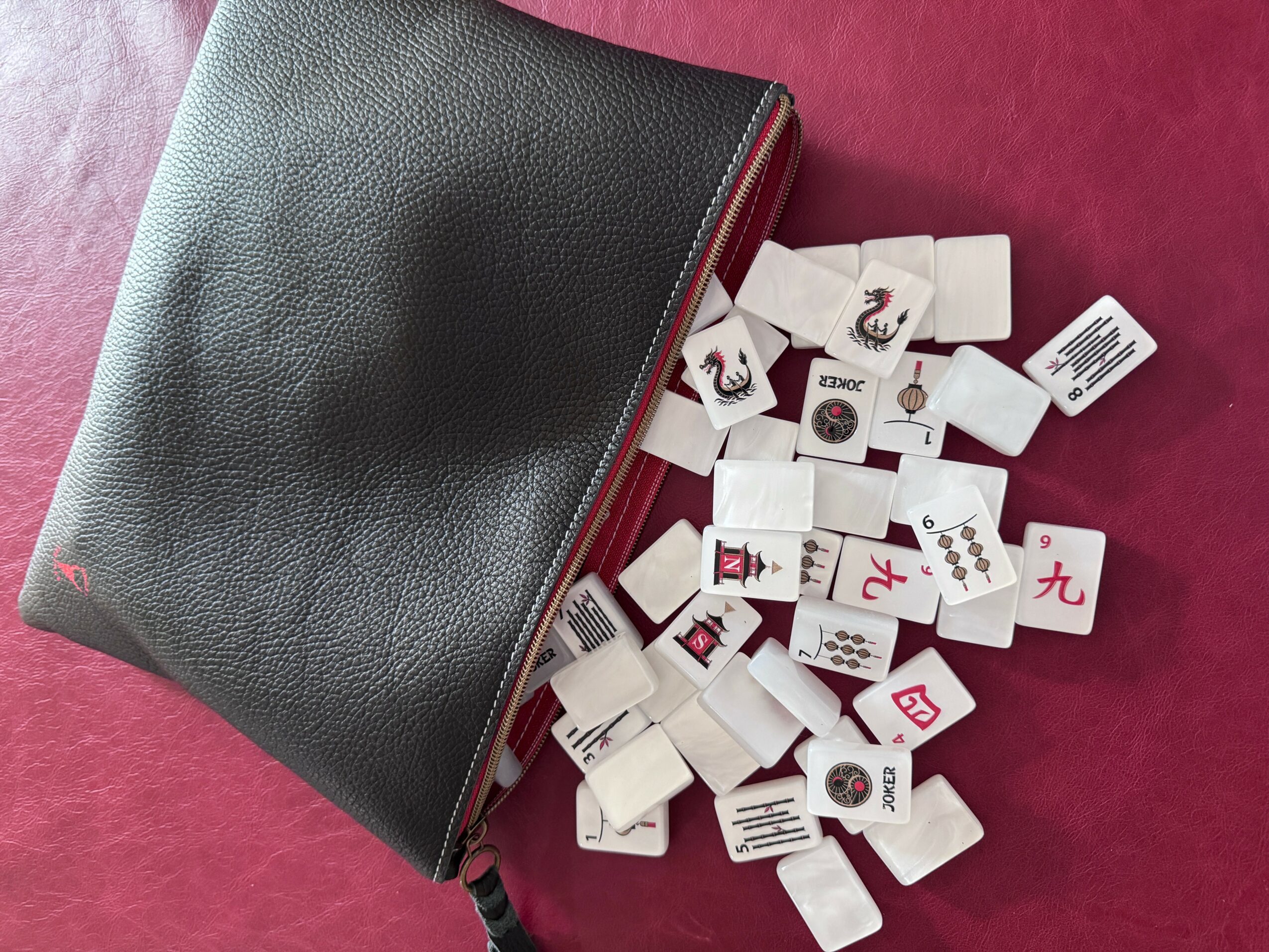 Black zippered pouch with scattered white tiles on a pink surface.