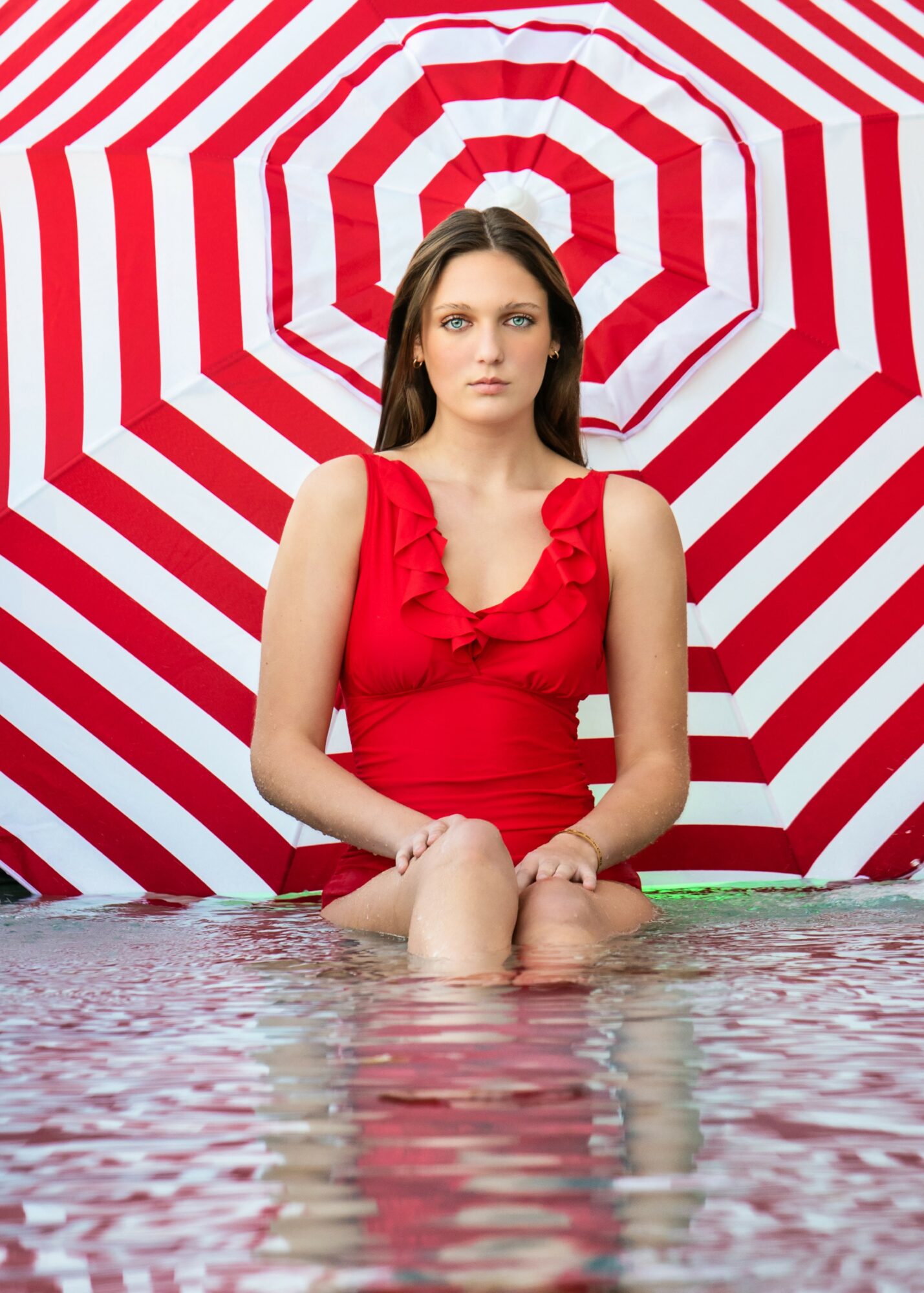 Woman in red dress sitting in water with a red and white striped umbrella background.