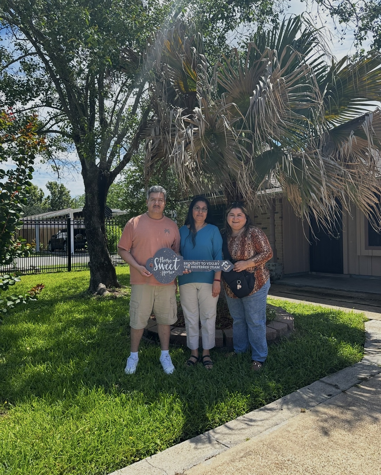 Three people standing outdoors on grass with trees and a building in the background.