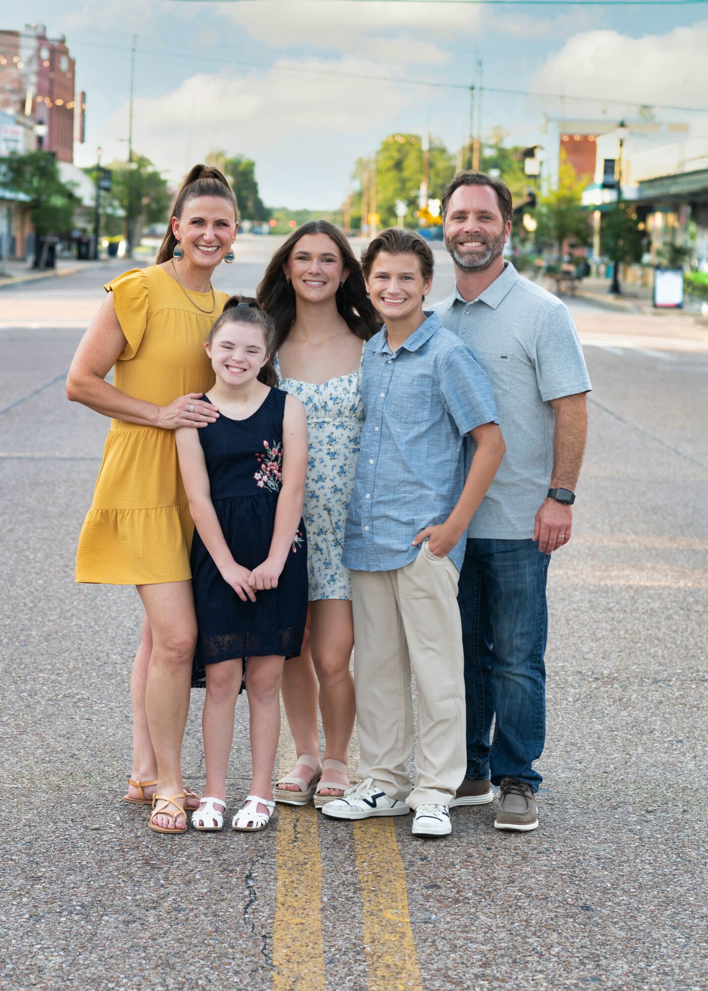 Group of five people standing on a city street, smiling, with buildings and trees in the background.