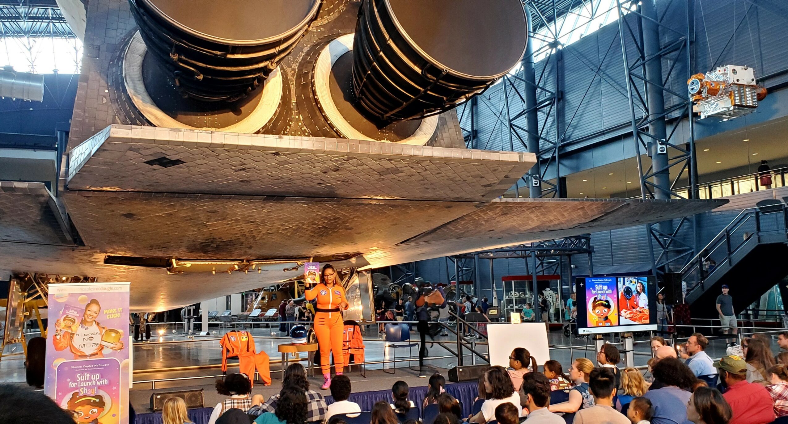 Large rocket model displayed indoors with people watching and informational screens nearby.